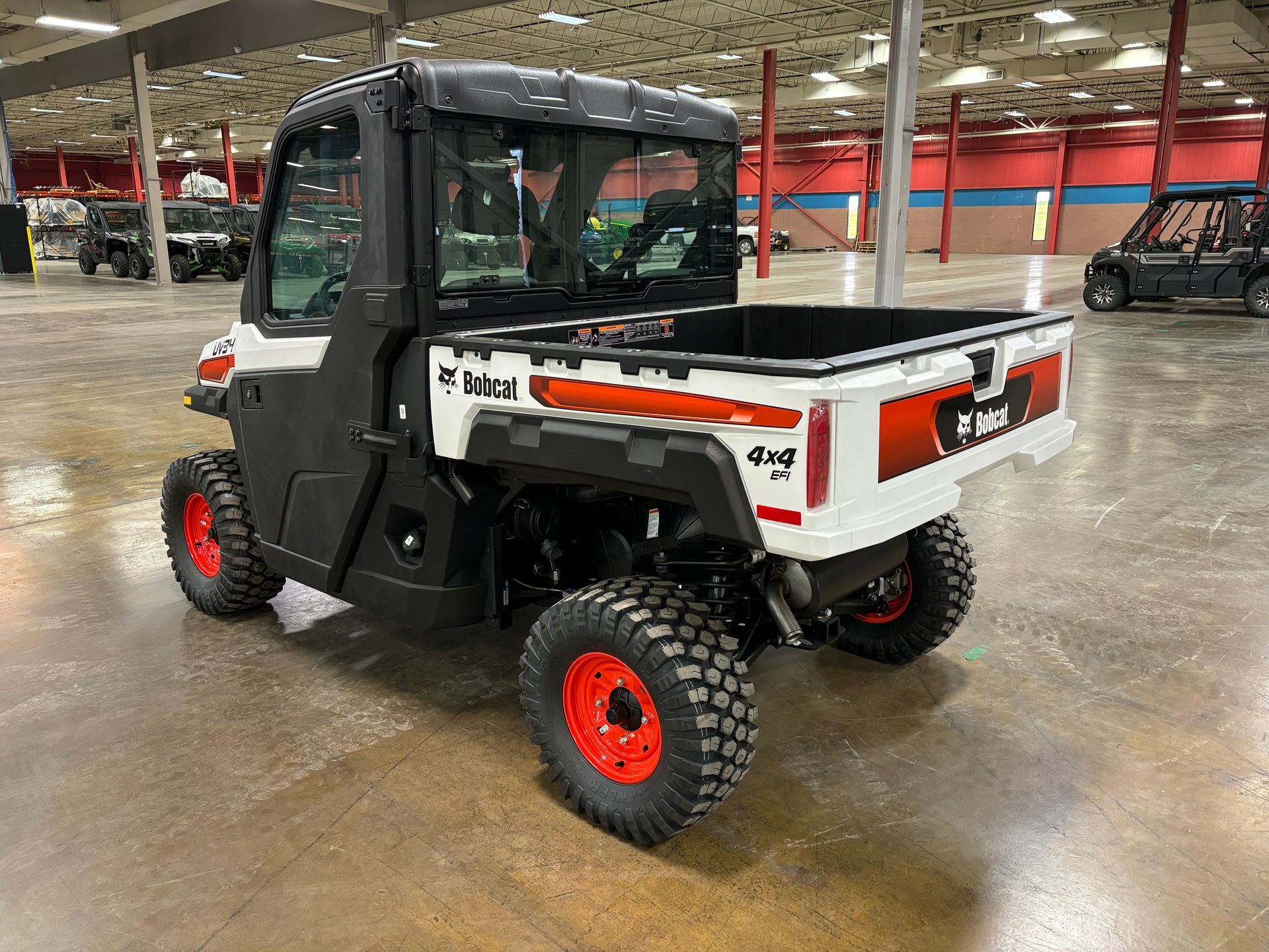 Bobcat utility vehicle, white and black with red wheels, parked indoors.