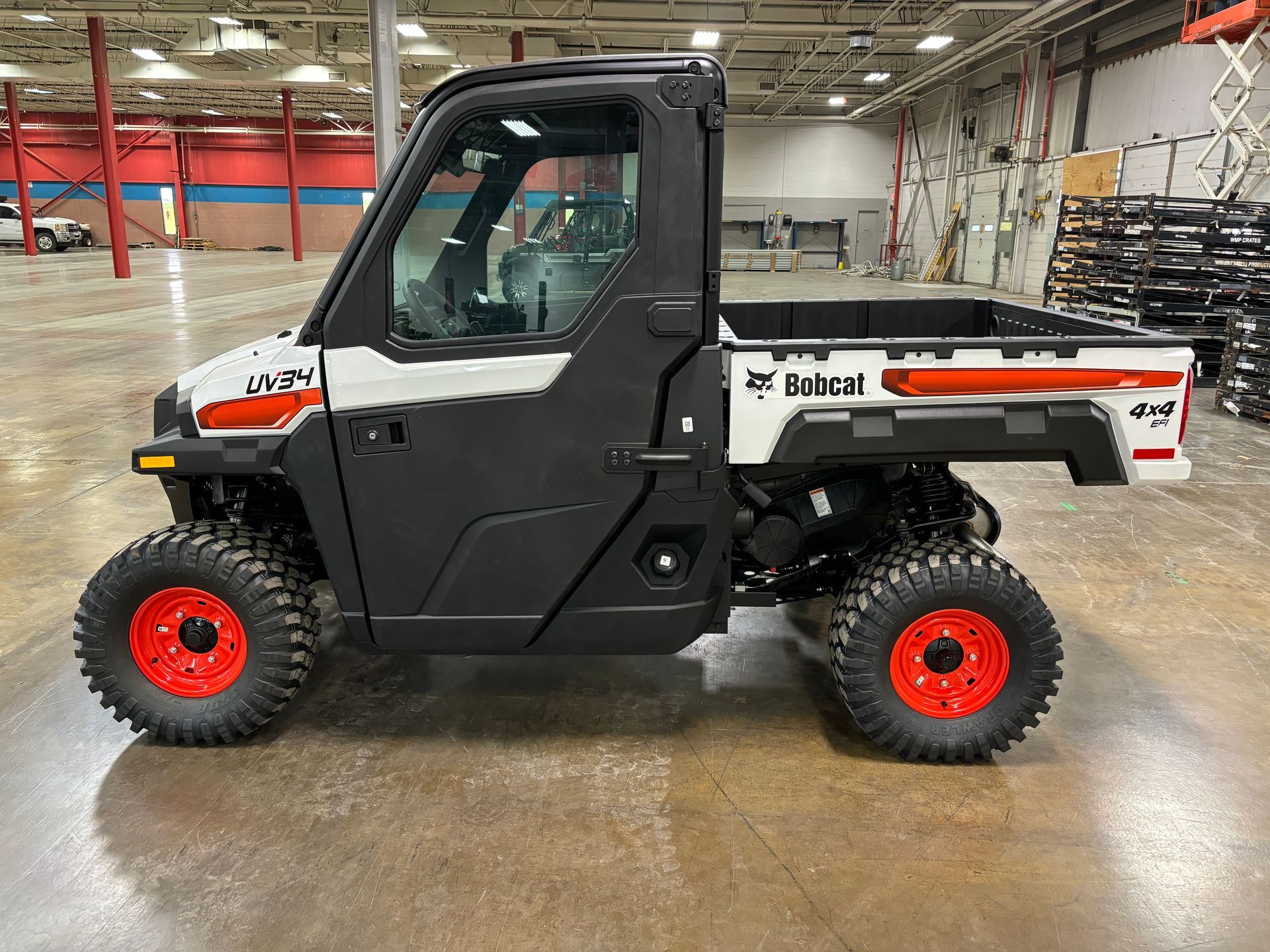 White and black Bobcat utility vehicle with red wheels and a bed, indoors.