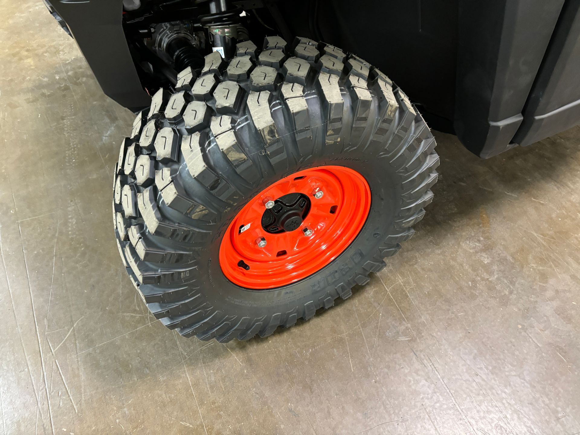 Close-up of an off-road vehicle tire with a black tire, orange rim, and a concrete floor.