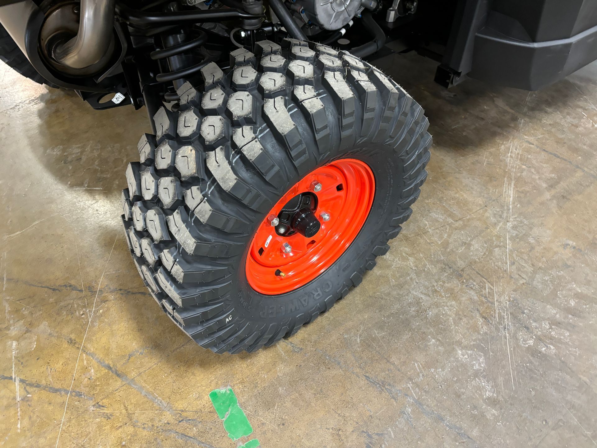 Close-up of a large ATV tire with a red rim, on a concrete surface.