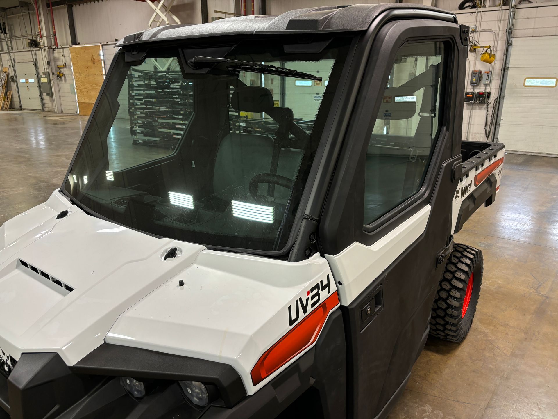 White and black utility vehicle with a windshield and cabin in a shop.