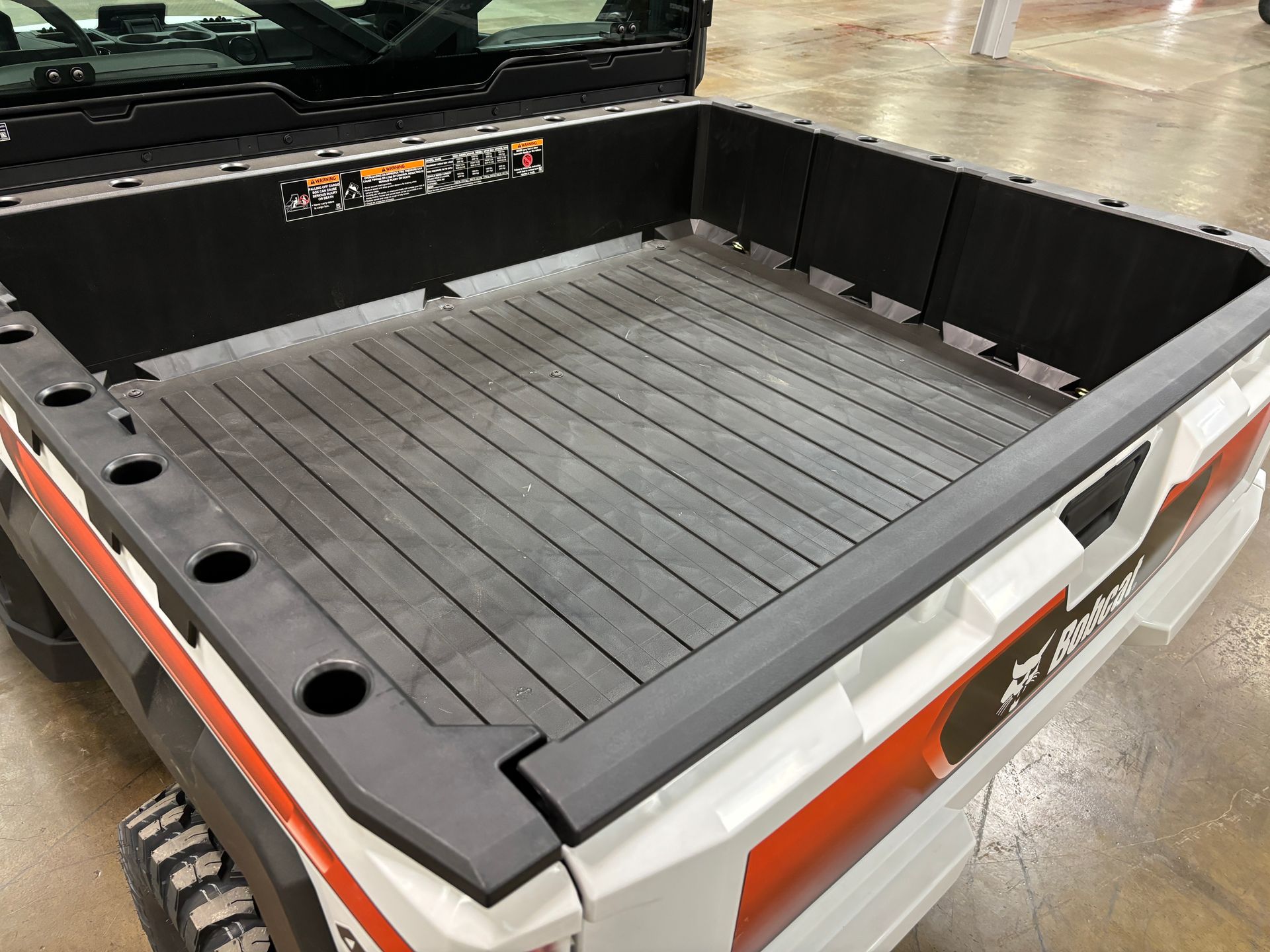 A white Bobcat utility vehicle bed with a black, ribbed floor and side rails.