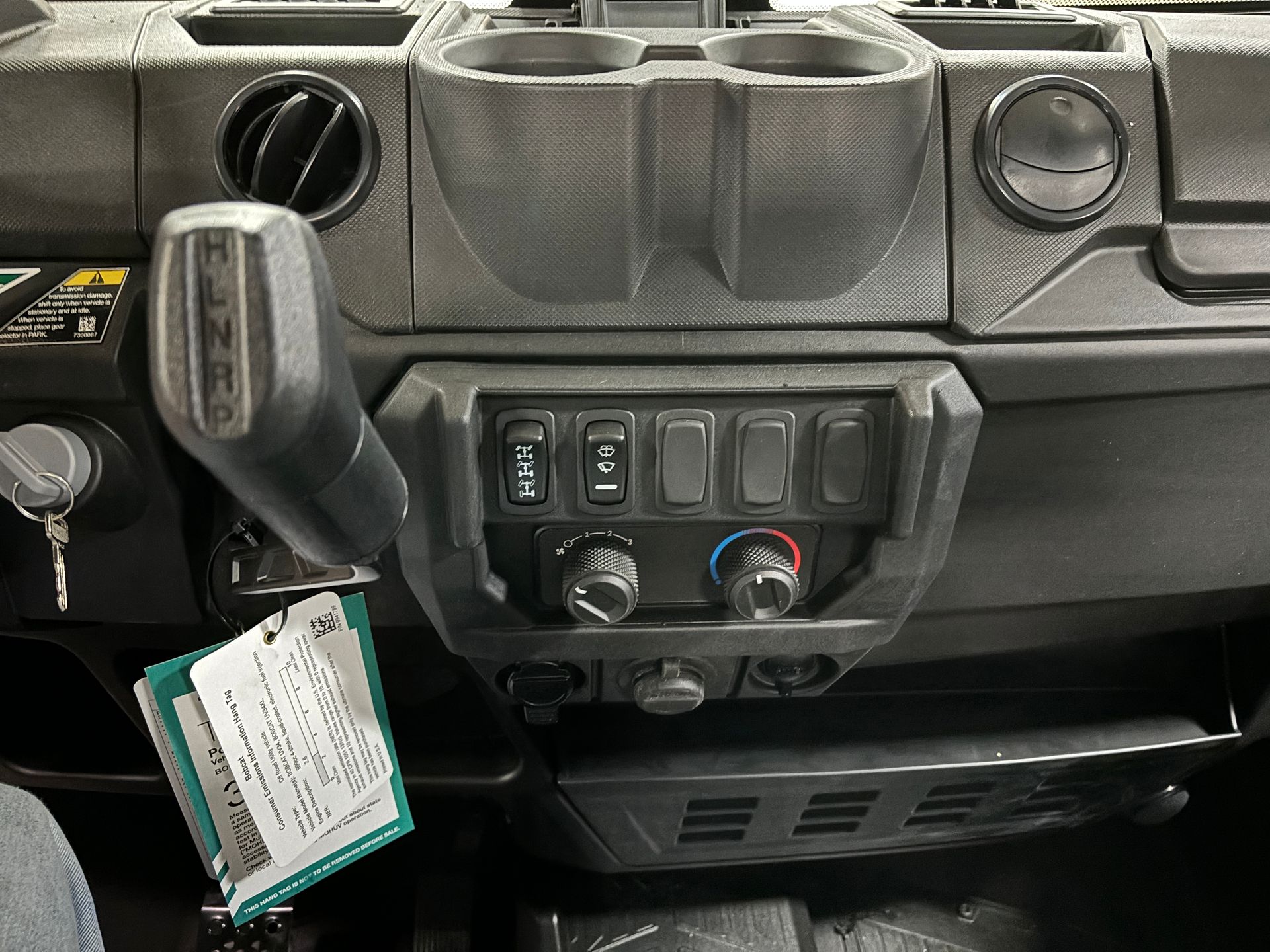 Dashboard of a vehicle, black with gear shift, buttons, dials, cup holders, and a shelf.