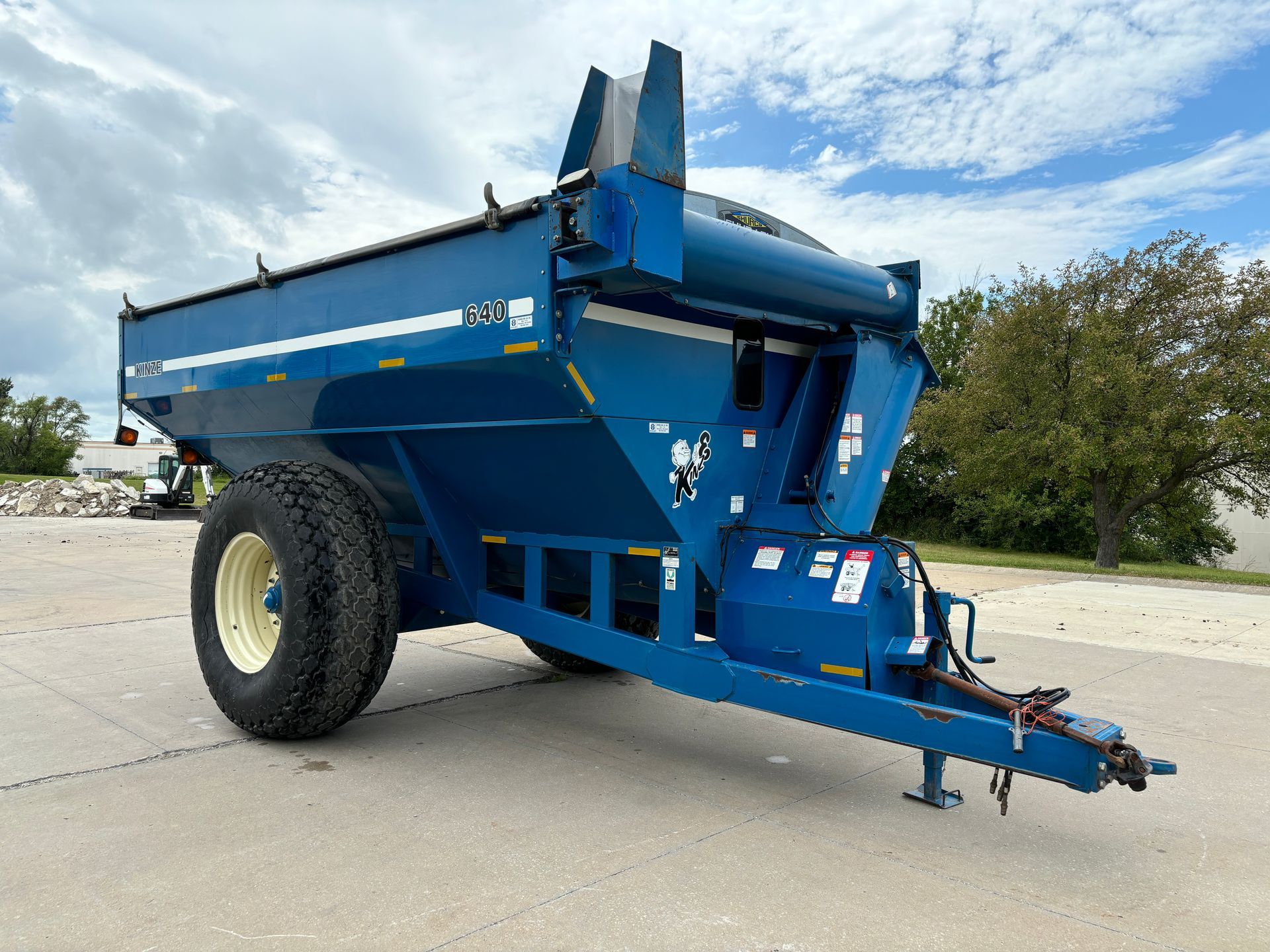 Blue agricultural grain cart on a paved surface with a sky in the background, front angled shot.