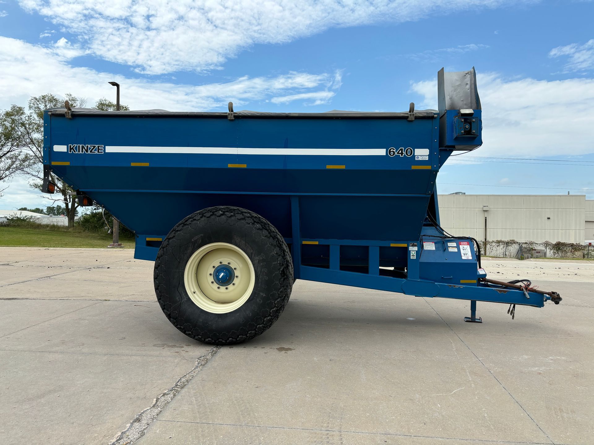 Blue agricultural grain cart on a paved surface with a sky in the background, side view shot.