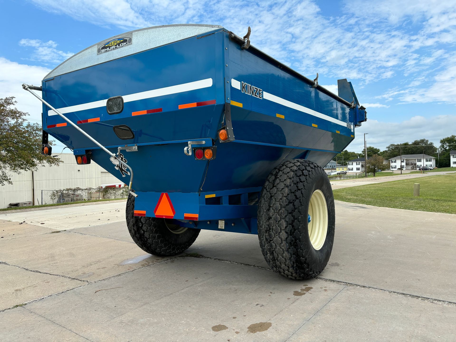 Blue agricultural grain cart on a paved surface with a sky in the background, back angled shot.