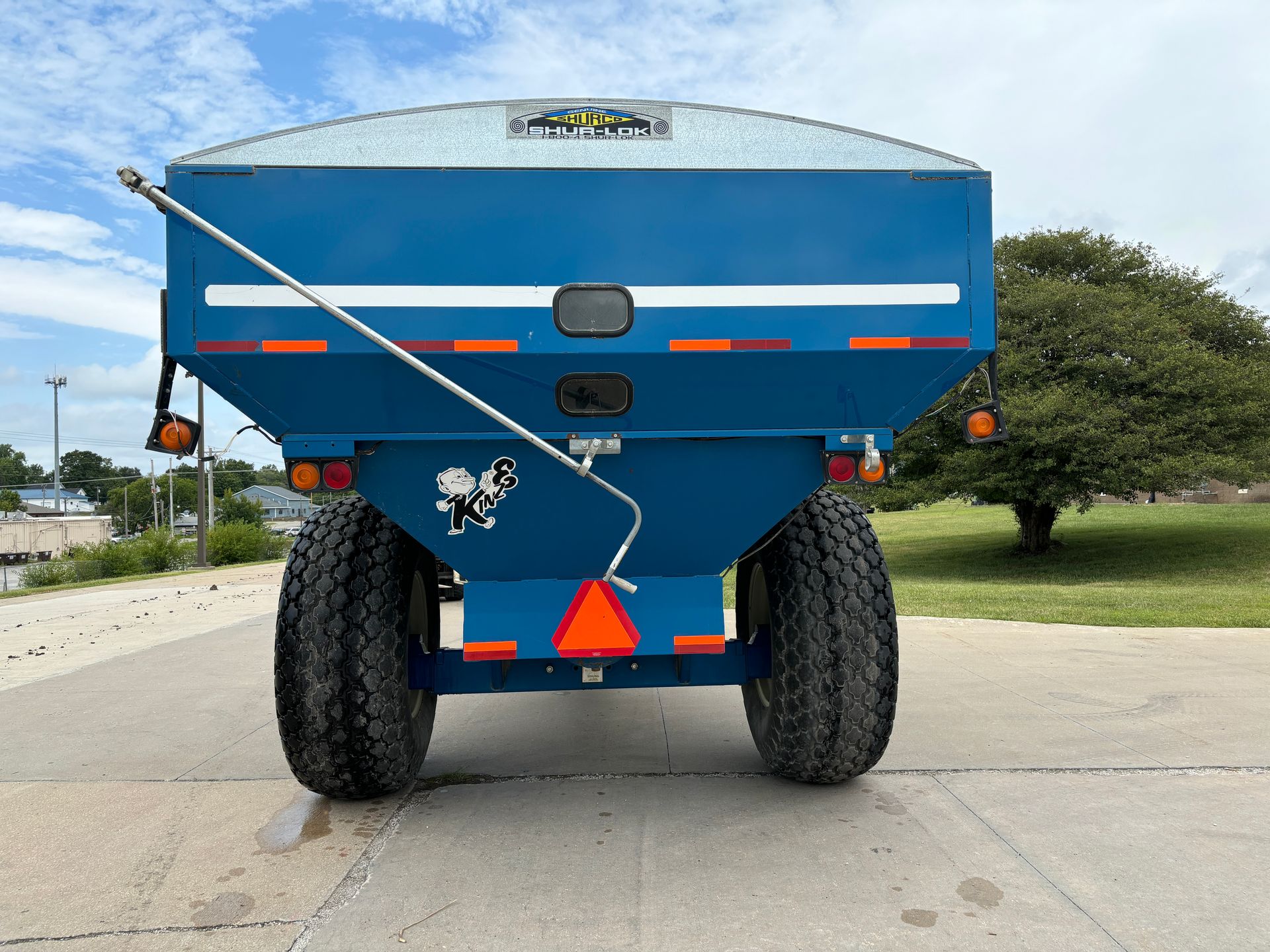 Blue agricultural grain cart on a paved surface with a sky in the background, back shot.