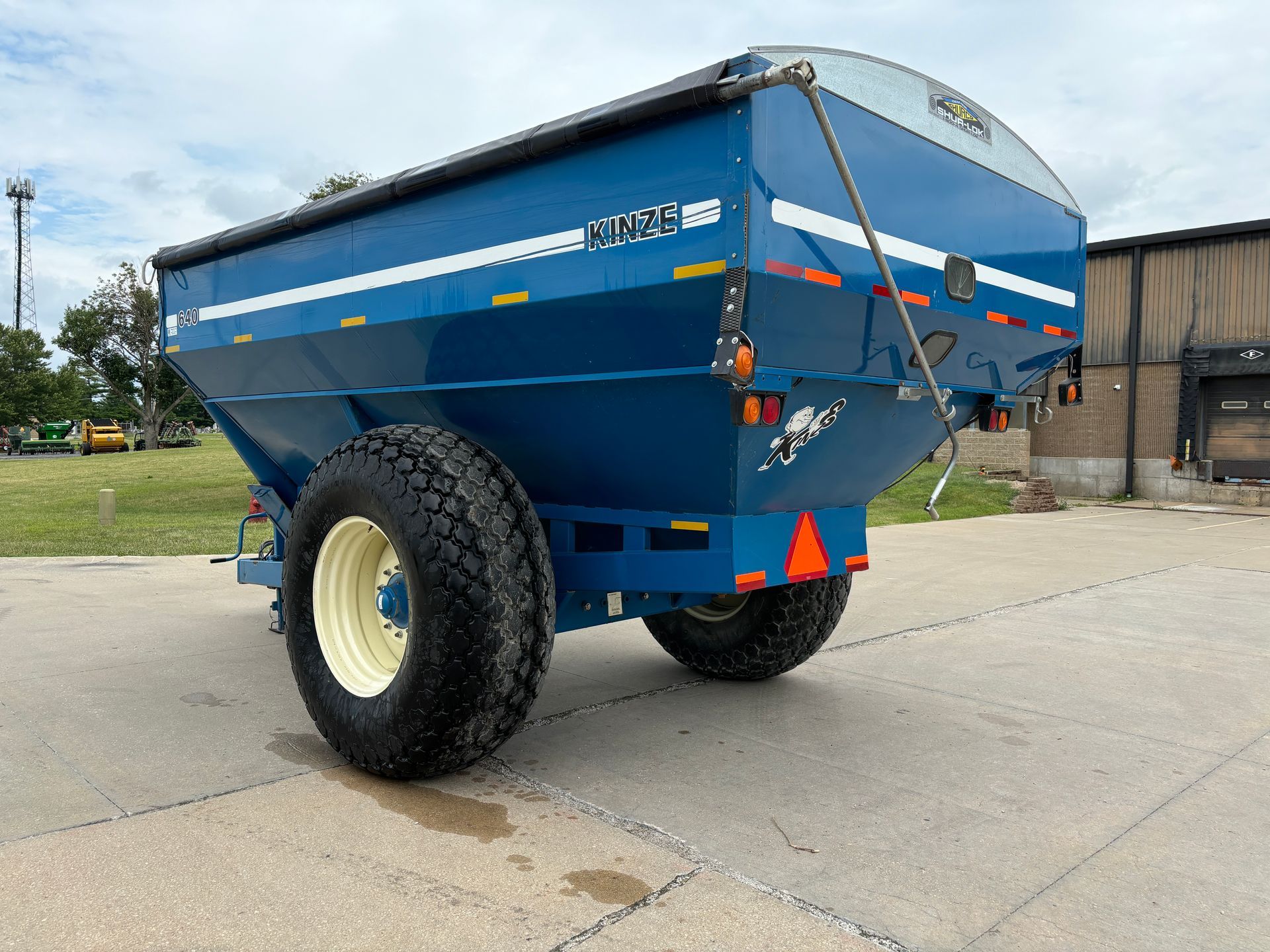 Blue agricultural grain cart on a paved surface with a sky in the background, back angled shot.