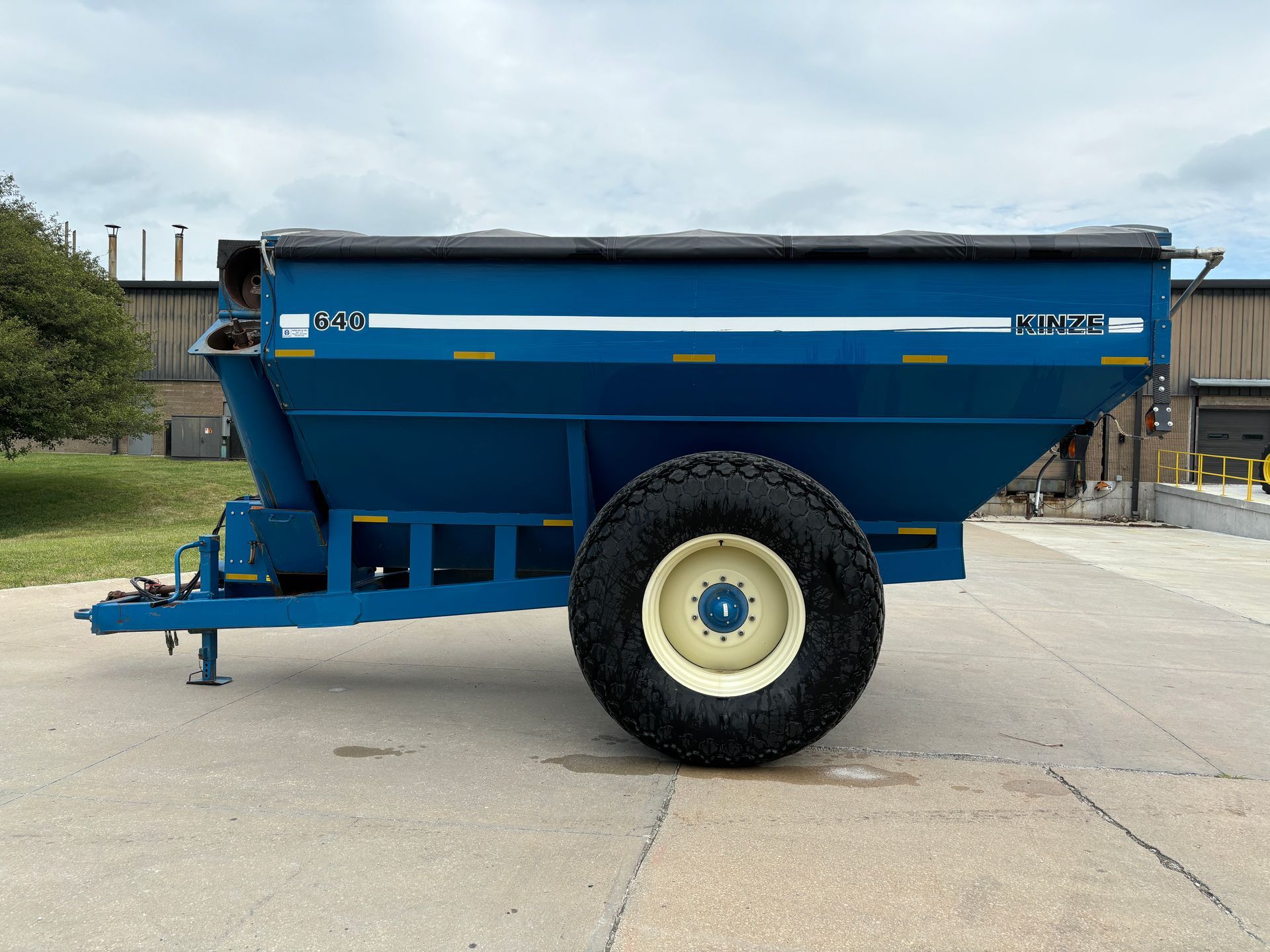 Blue agricultural grain cart on a paved surface with a sky in the background, side view shot.