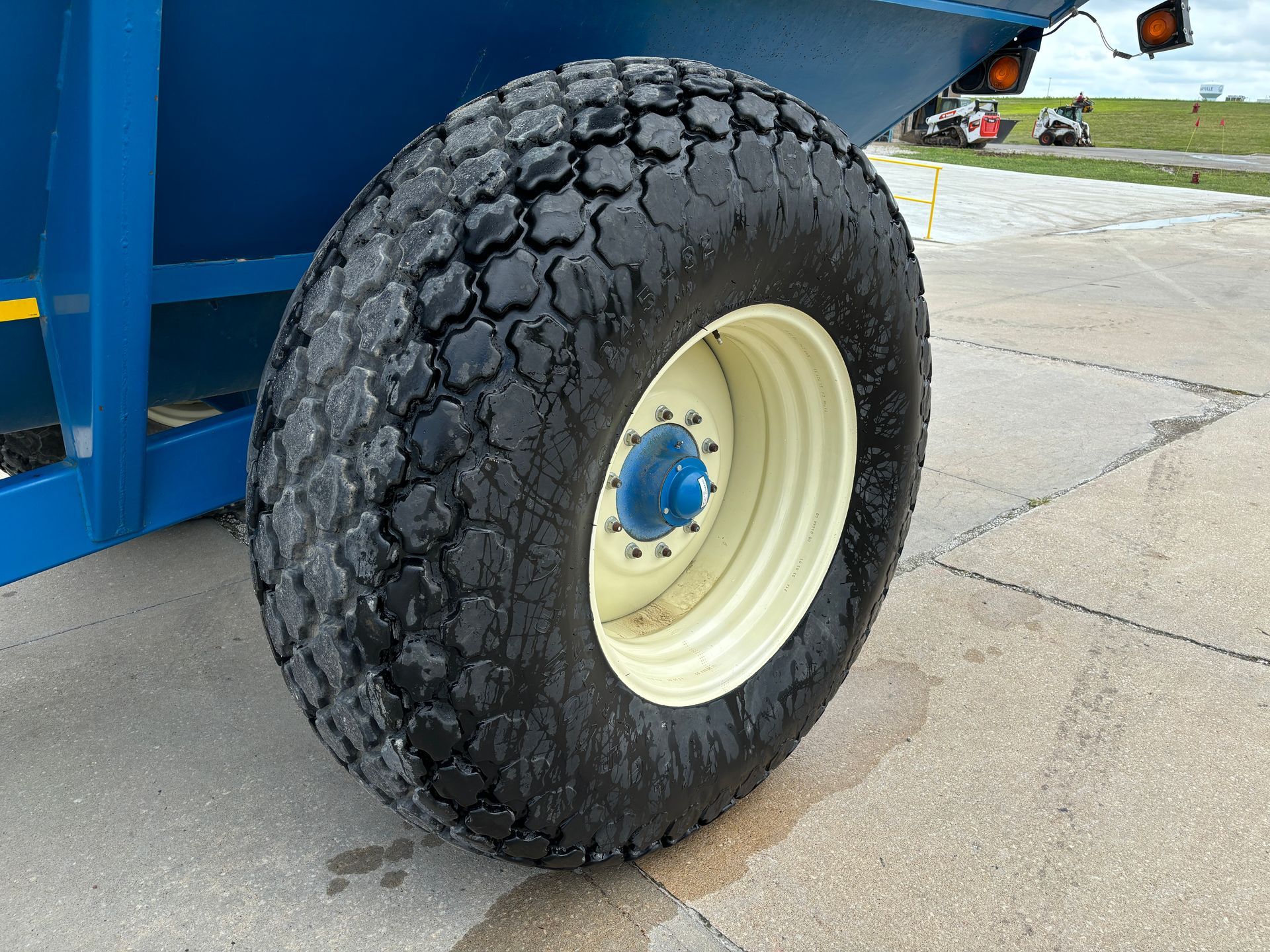 A large, black, worn tire on a cream-colored rim with a blue hub, attached to a blue grain cart.