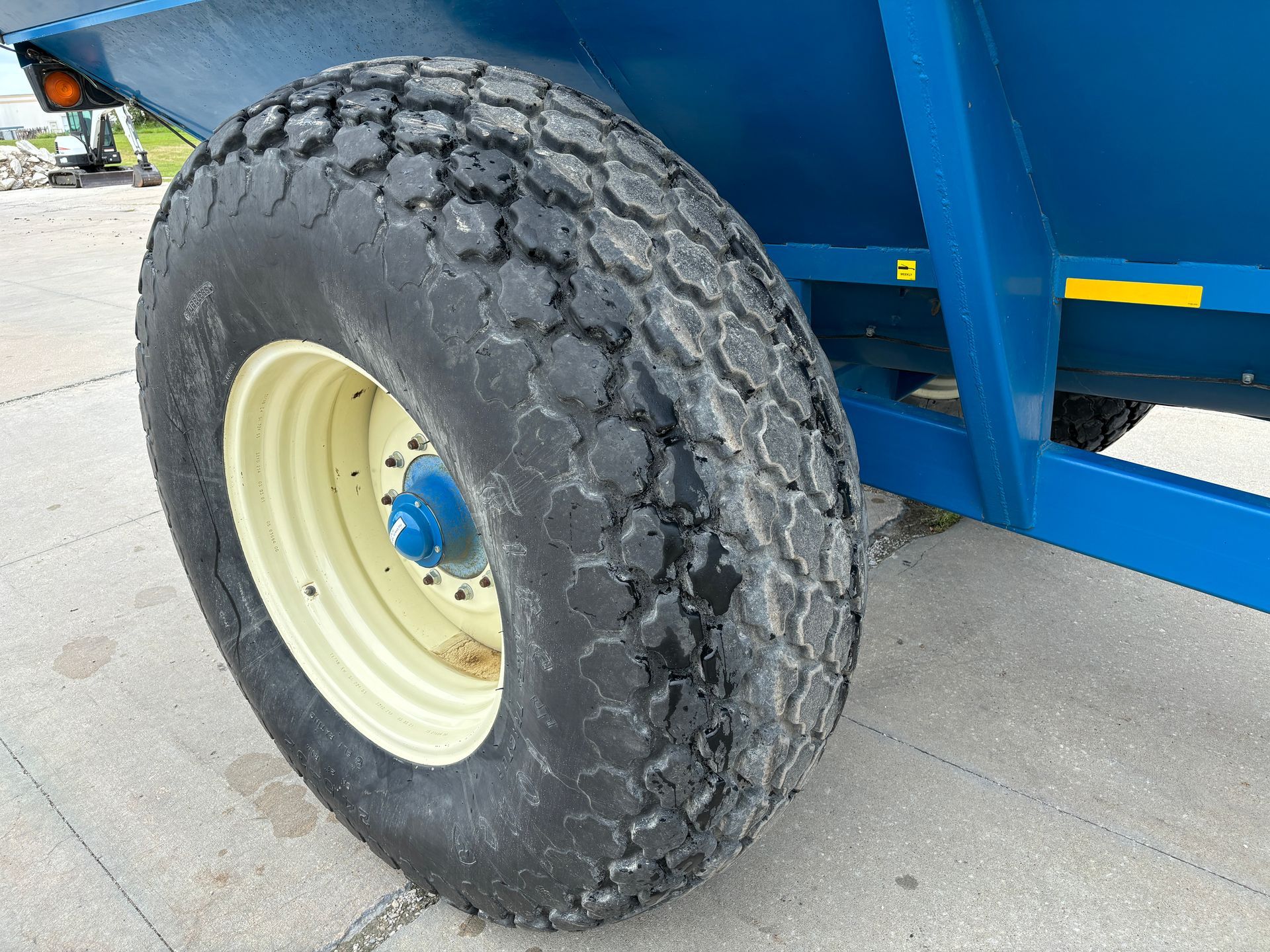 A large, black, worn tire on a cream-colored rim with a blue hub, attached to a blue grain cart.