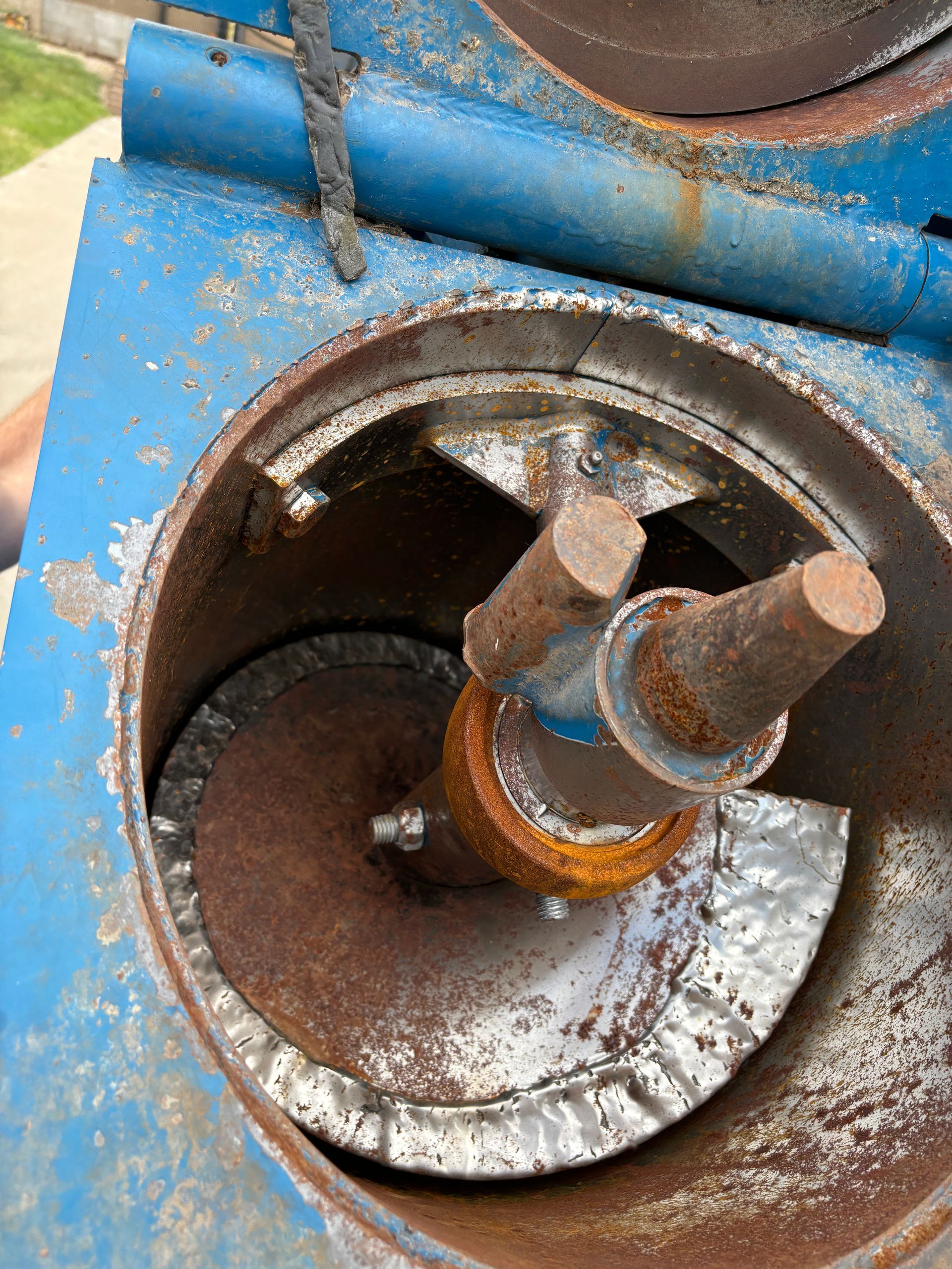 Inside of a rusty blue machine with spiral blades and rotating metal rods.