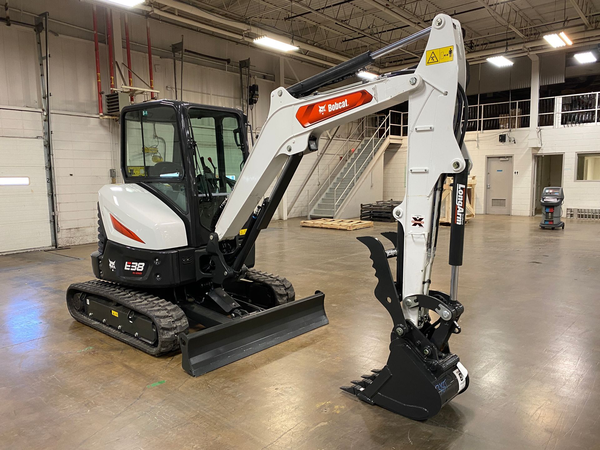 Bobcat excavator, white and black, indoors, bucket raised.