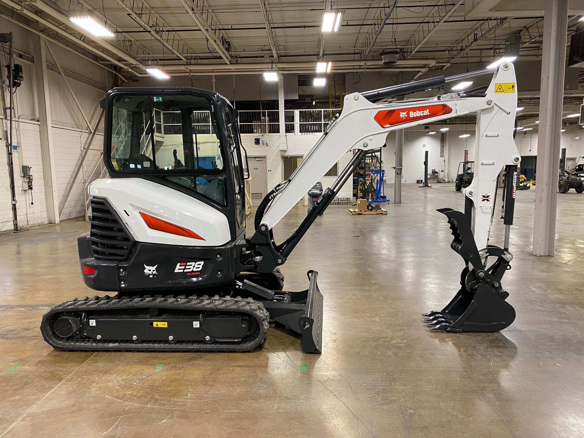 White Bobcat excavator in a warehouse, arm extended with bucket.