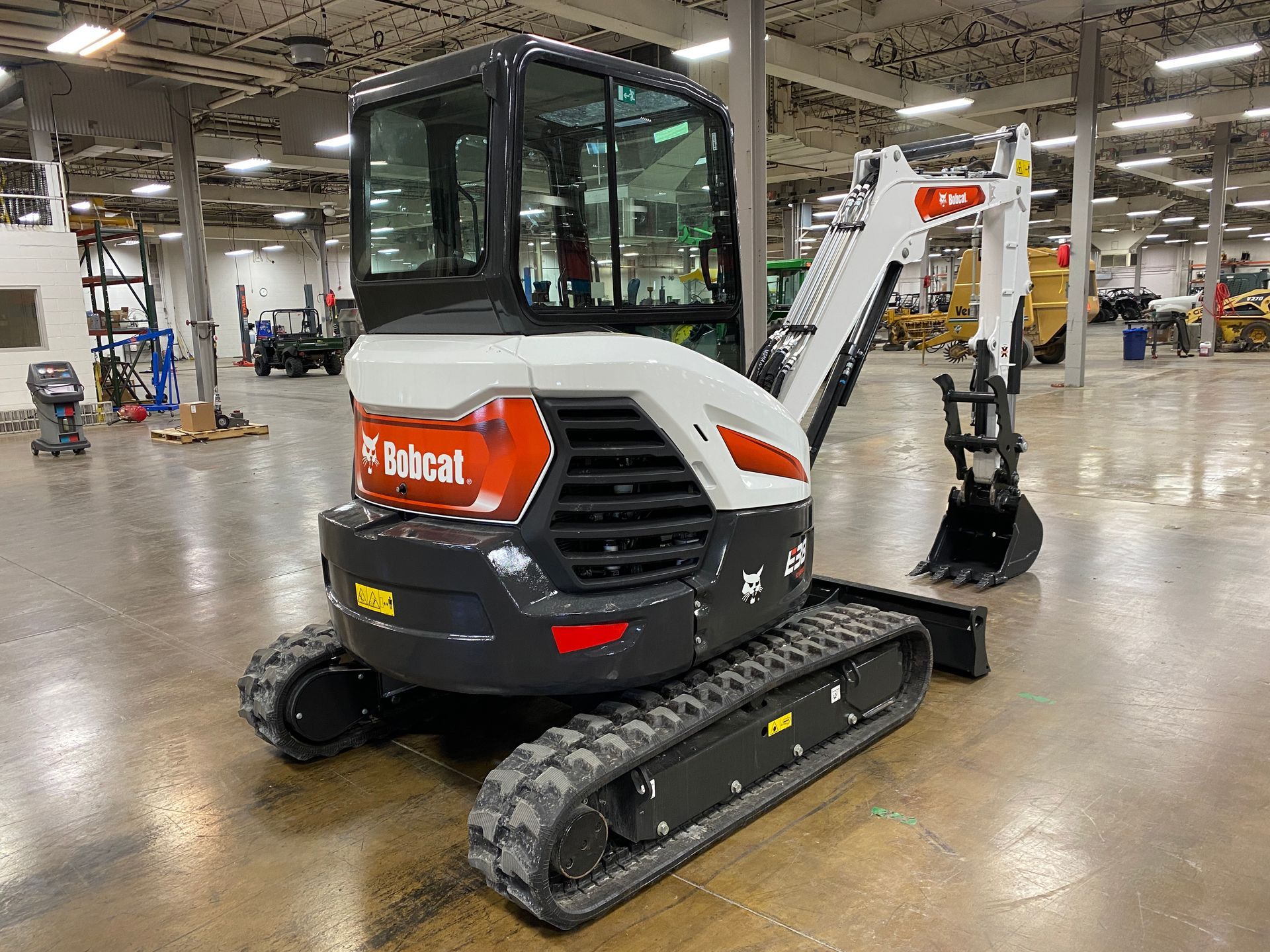 Bobcat E42 mini excavator on a concrete floor in a large indoor setting. White and black with orange logo.