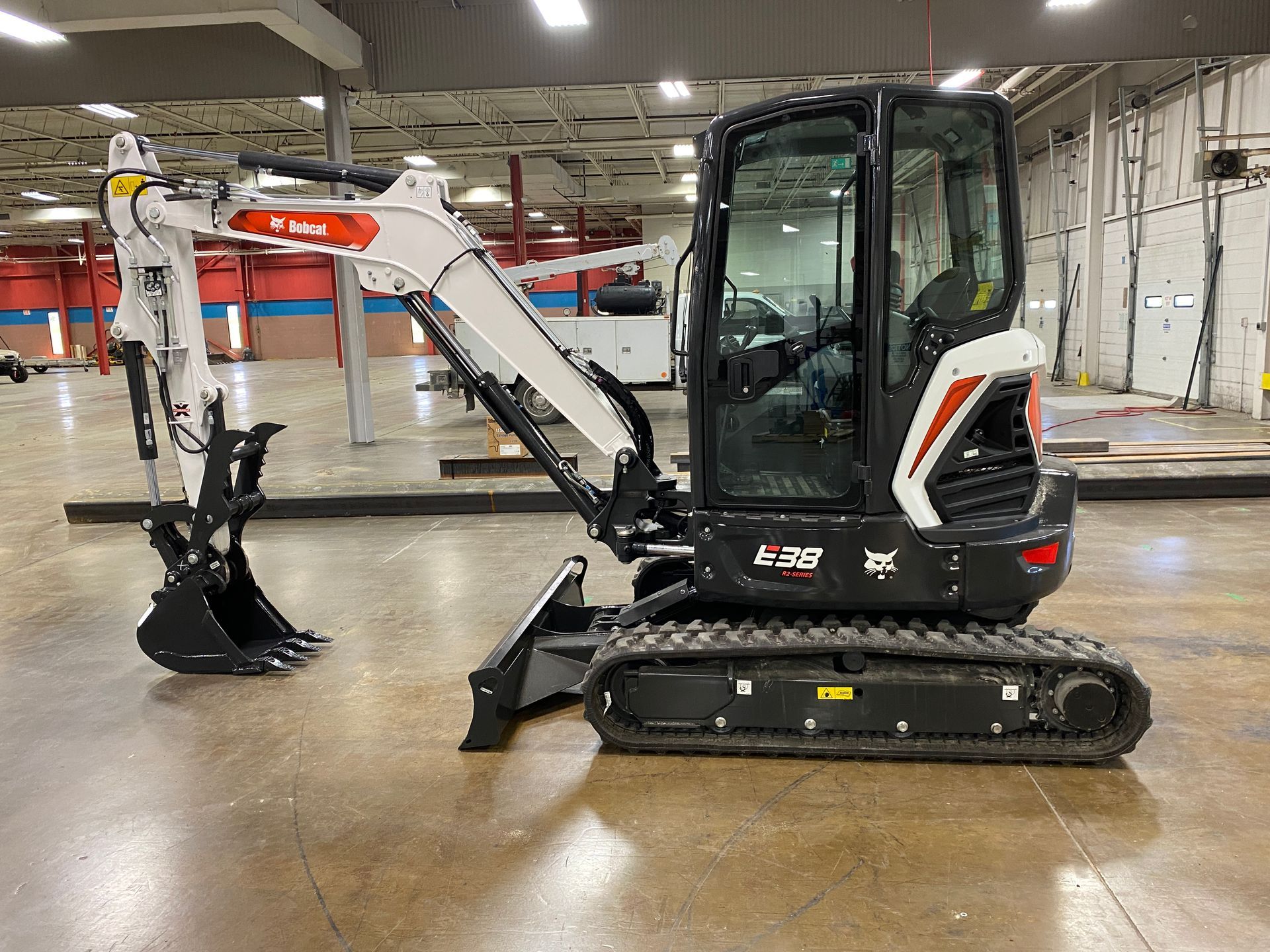 Bobcat E26 compact excavator in a warehouse setting, with arm extended and bucket down.