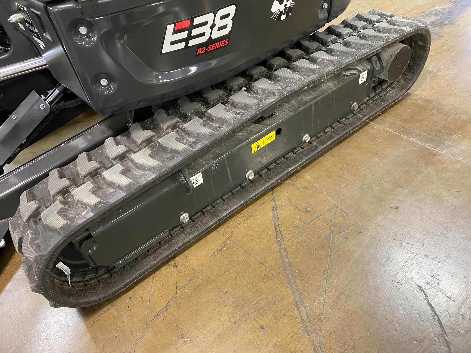 Black Bobcat E38 mini excavator track on concrete floor.