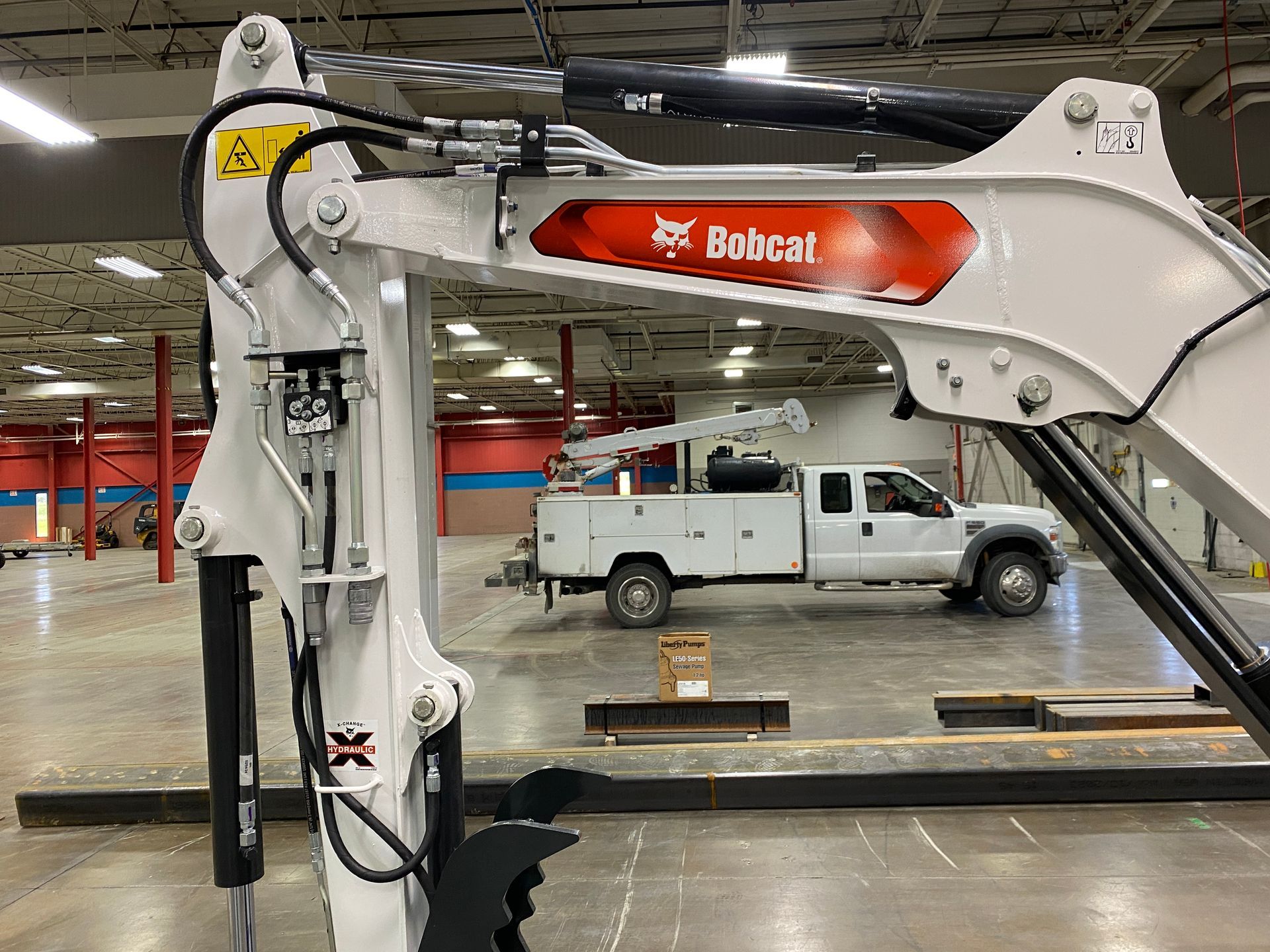 Bobcat excavator arm, with logo, in warehouse setting with white work truck.