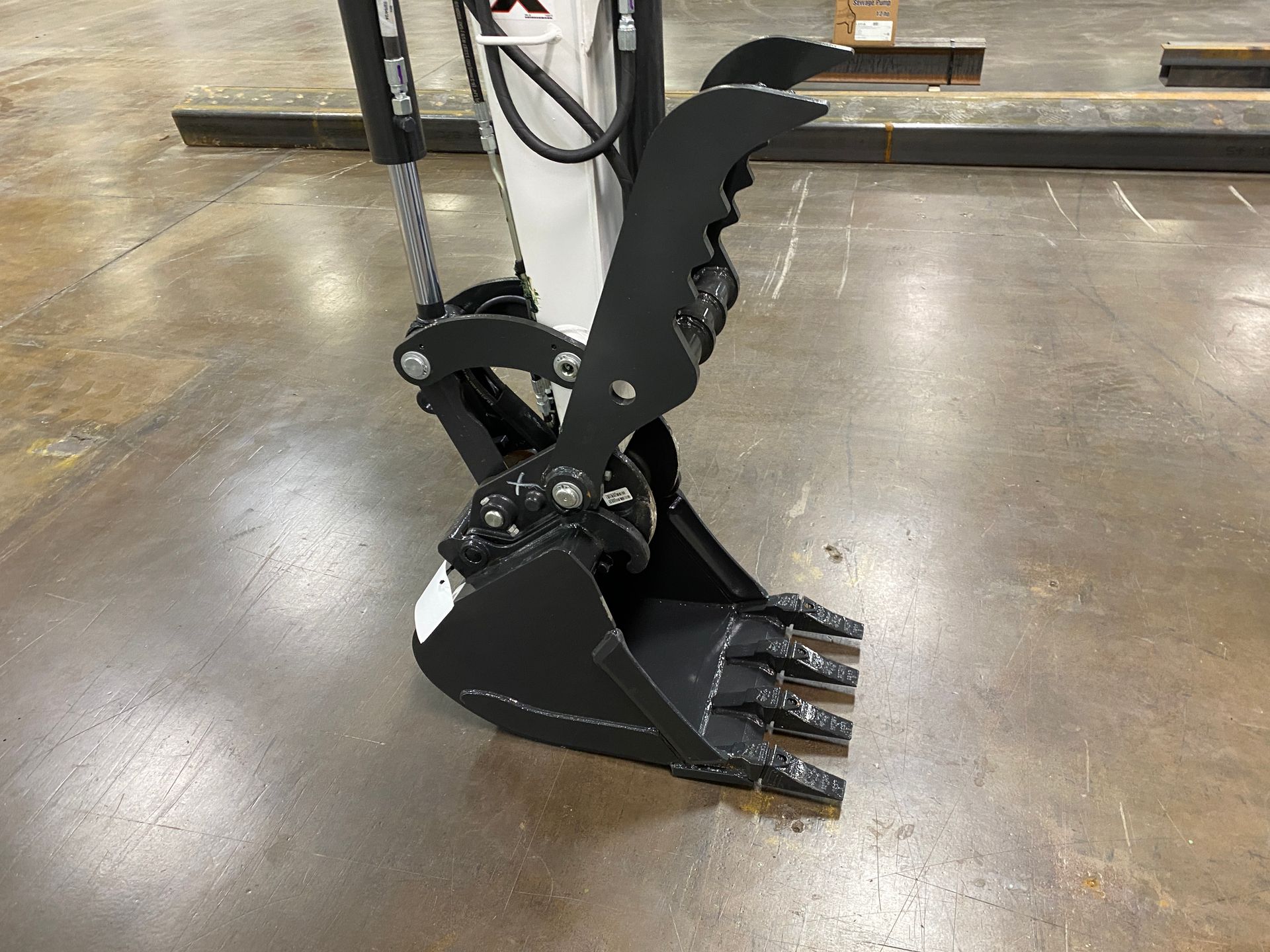 Black excavator bucket with grapple claw attachment on a gray floor.