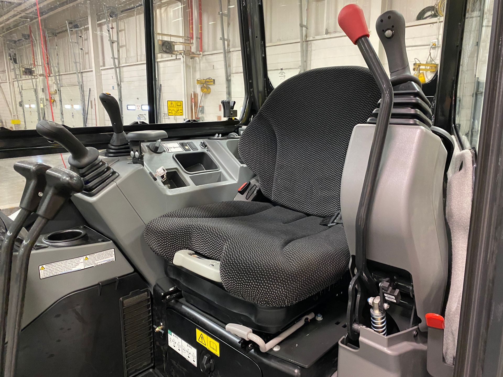 Interior of an excavator cab with seat, controls, and levers. Gray and black.