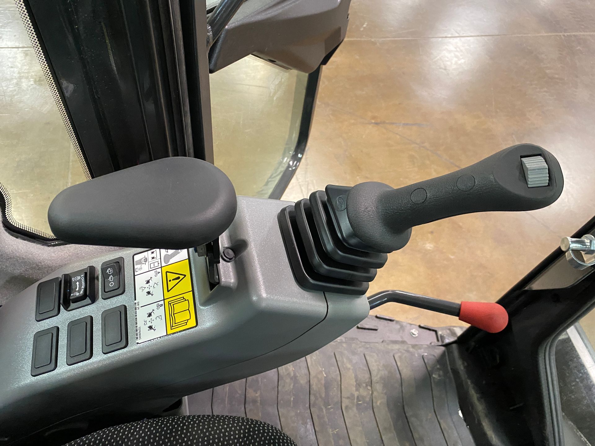 Control panel with joystick and buttons inside an excavator cab.