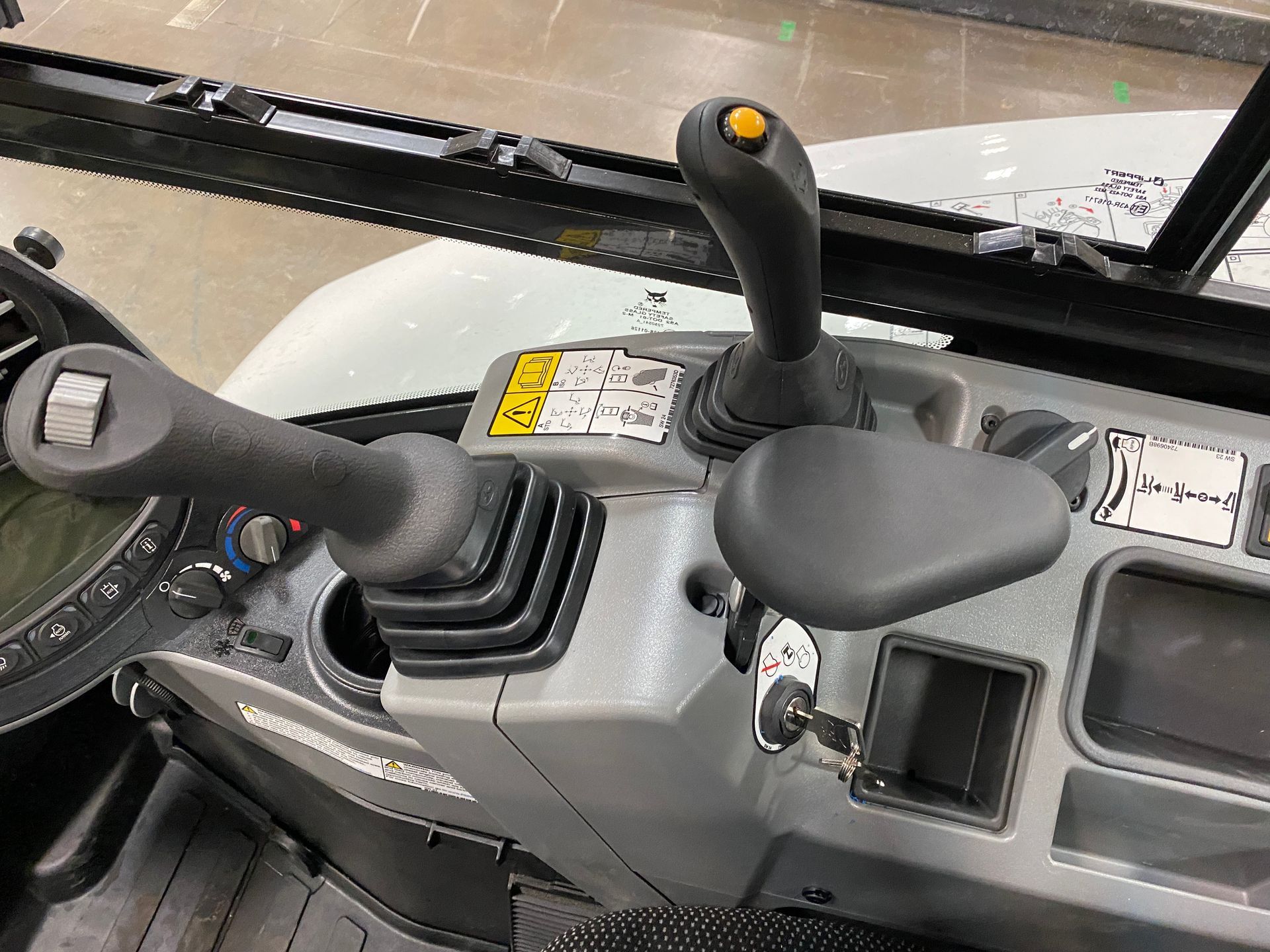 Interior view of a construction vehicle cabin, showing control sticks, a seat, and a dashboard.