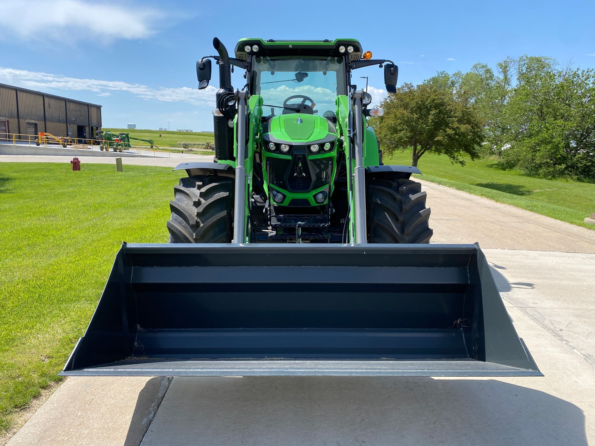 Green and black tractor with a front bucket parked on pavement in front of a building.
