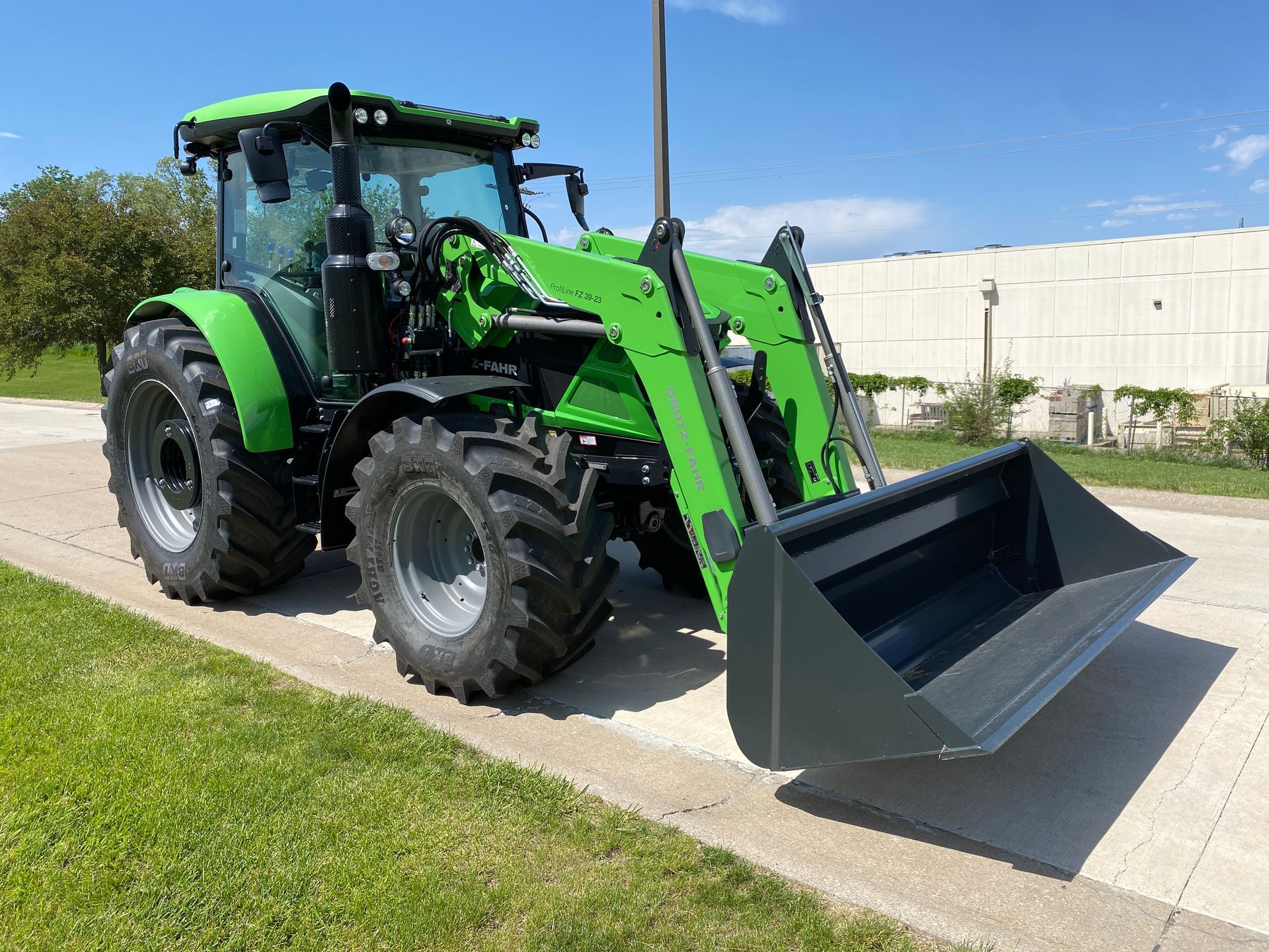 Green tractor with front-end loader on a paved surface, sunny day.