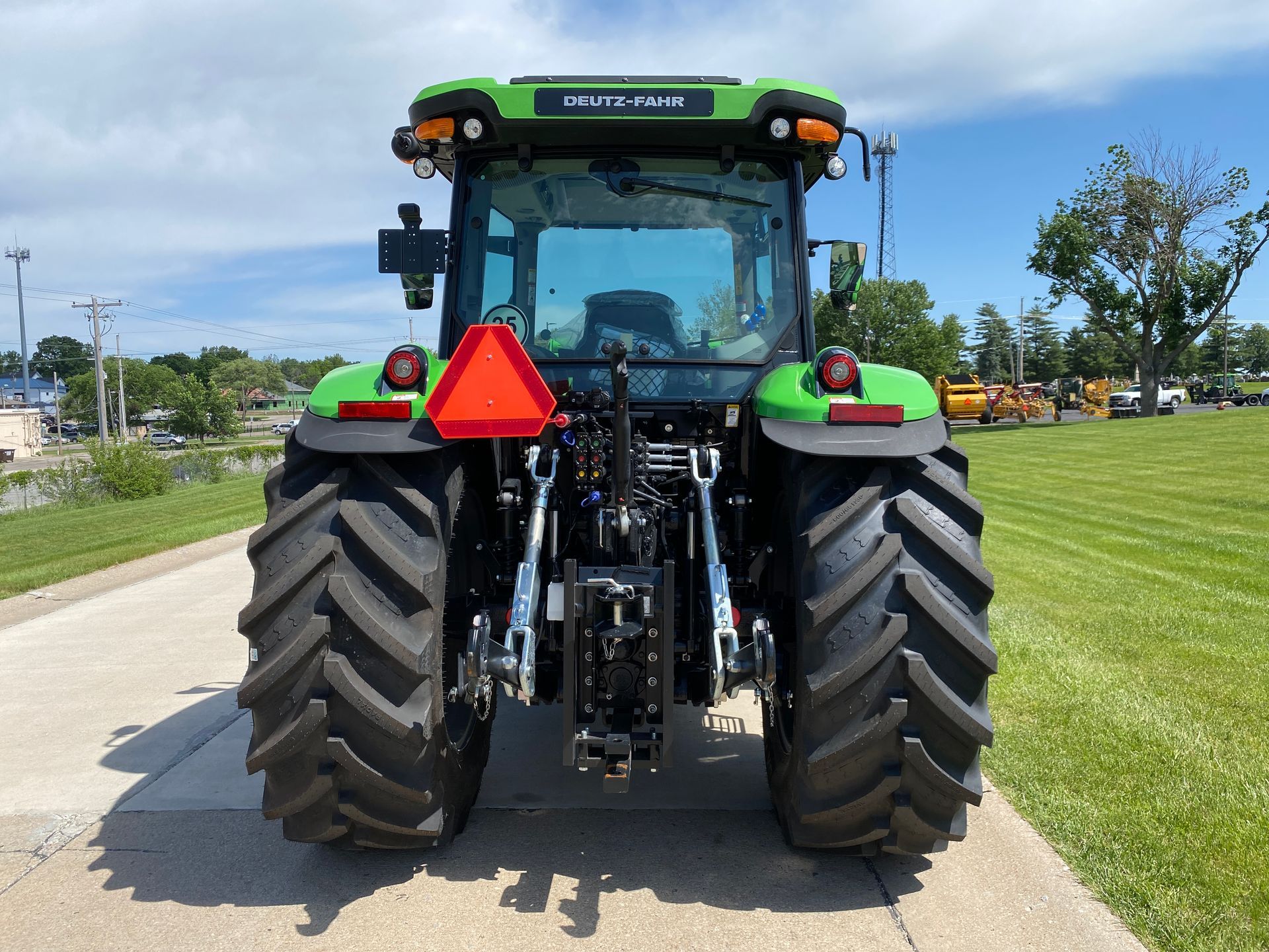Rear view of a green and black Deutz-Fahr tractor with large tires, orange triangle, and a clear sky.