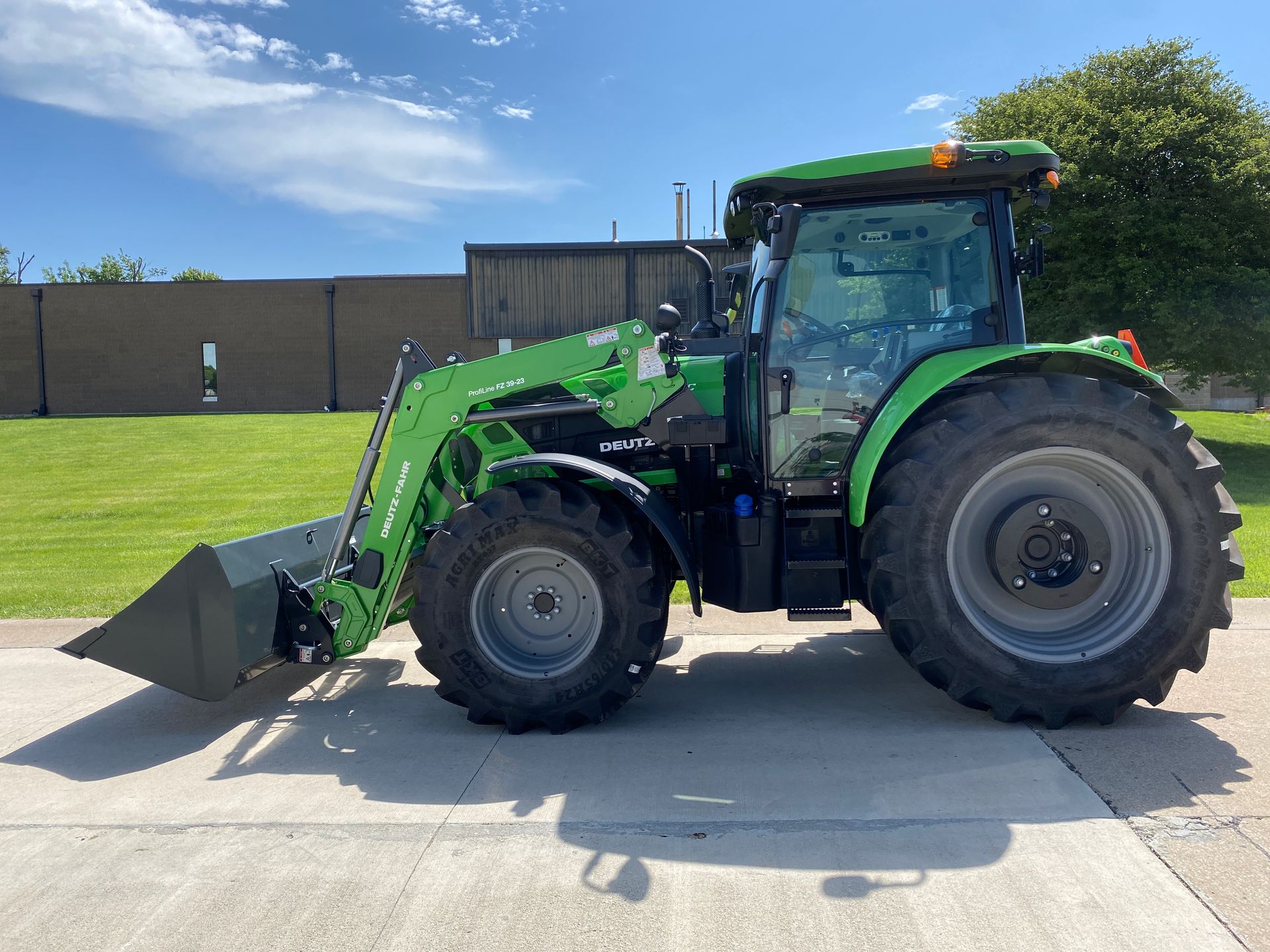 Green tractor with a front loader on paved surface.