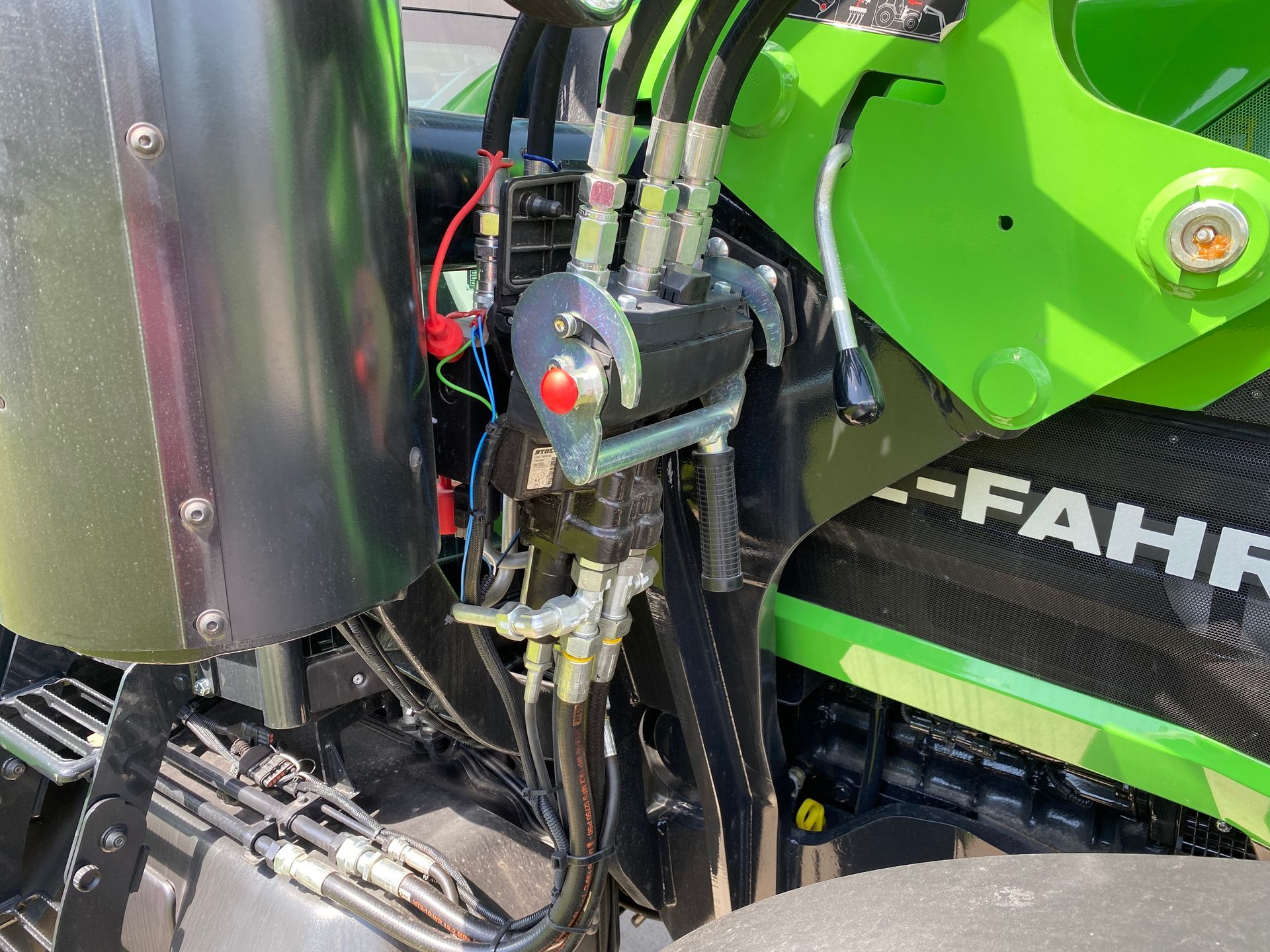 Hydraulic control system with black hoses and a red emergency stop button on a green tractor.