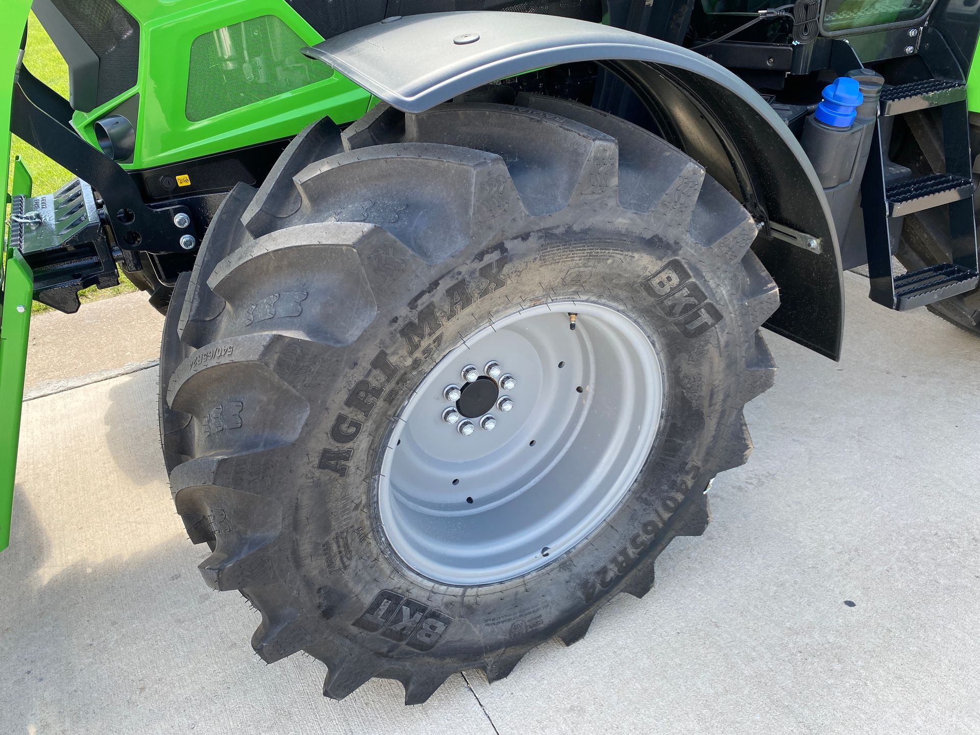Large tractor wheel with black tire and silver rim, under a black fender.