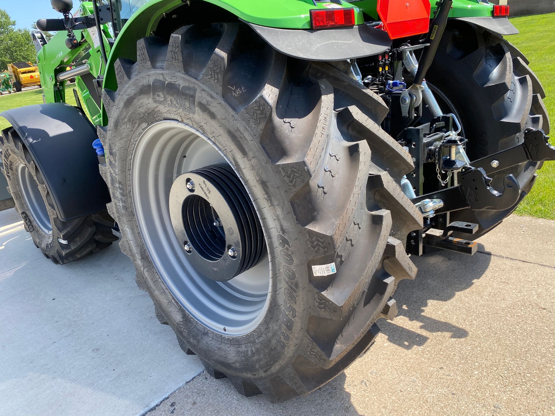 Rear view of a green tractor with large tires on pavement.