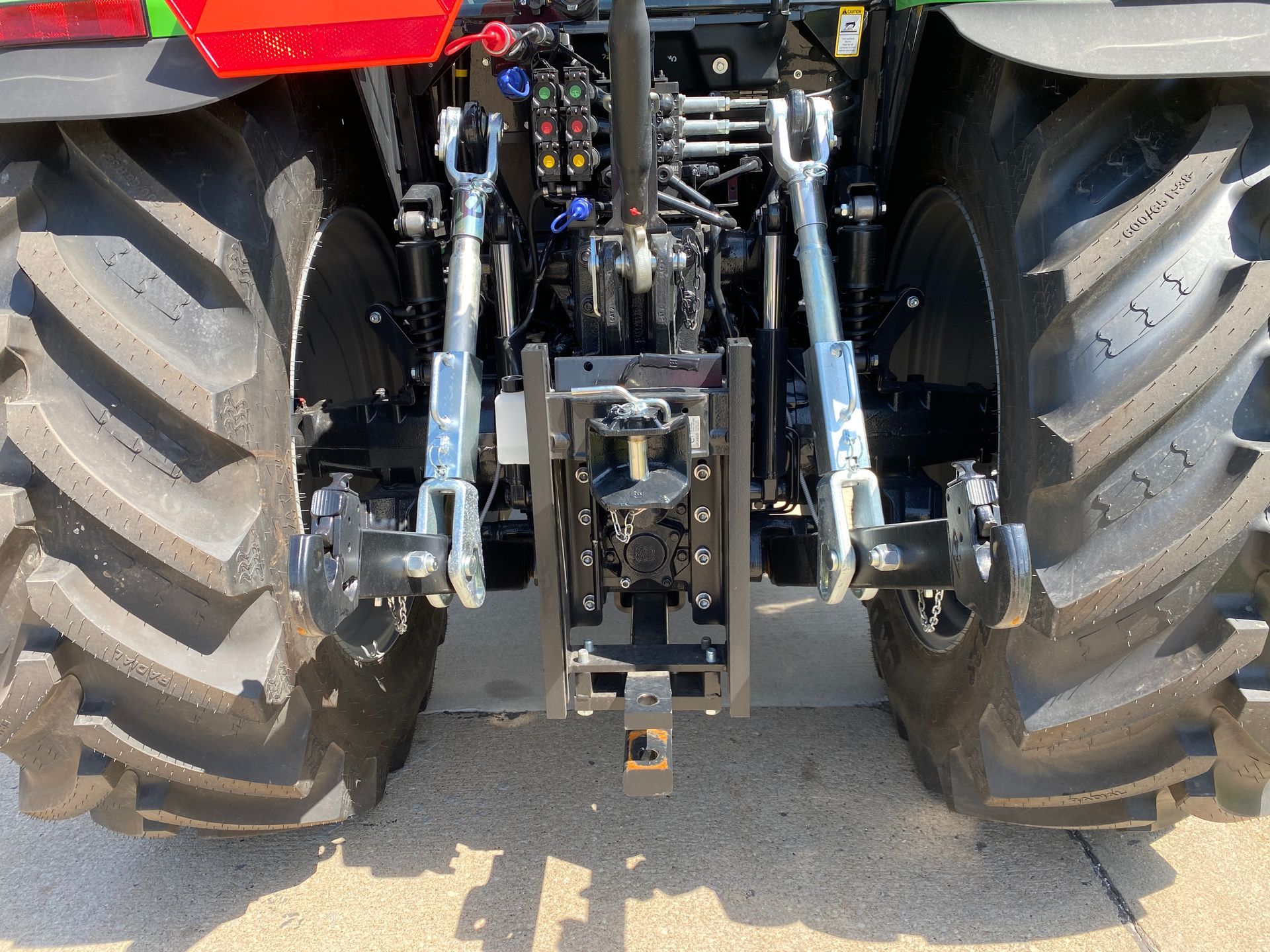 Rear view of a green tractor, showing large tires, hitch, and lifting arms.