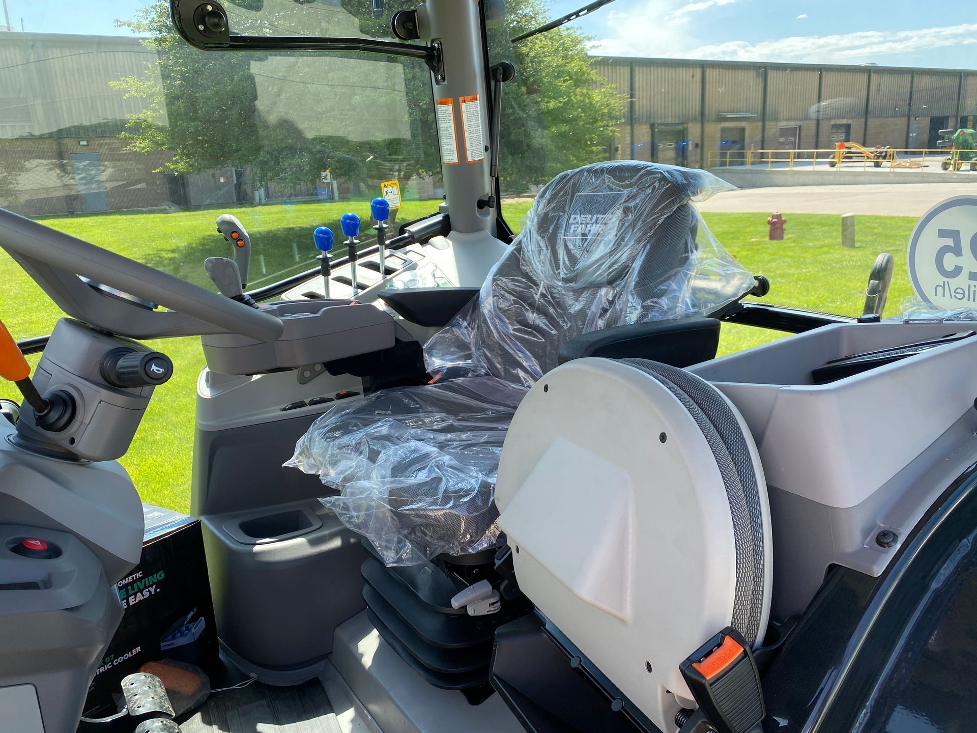 Interior view of tractor cab, seat covered in plastic, with controls and windows.