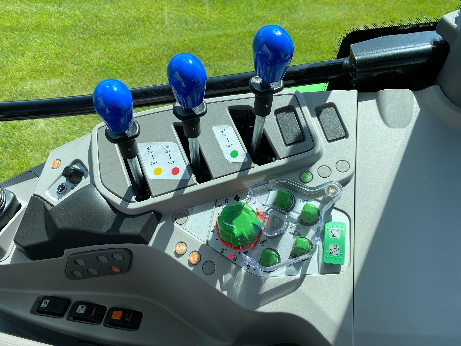 Dashboard controls of a tractor with blue and green levers and buttons on a gray console.
