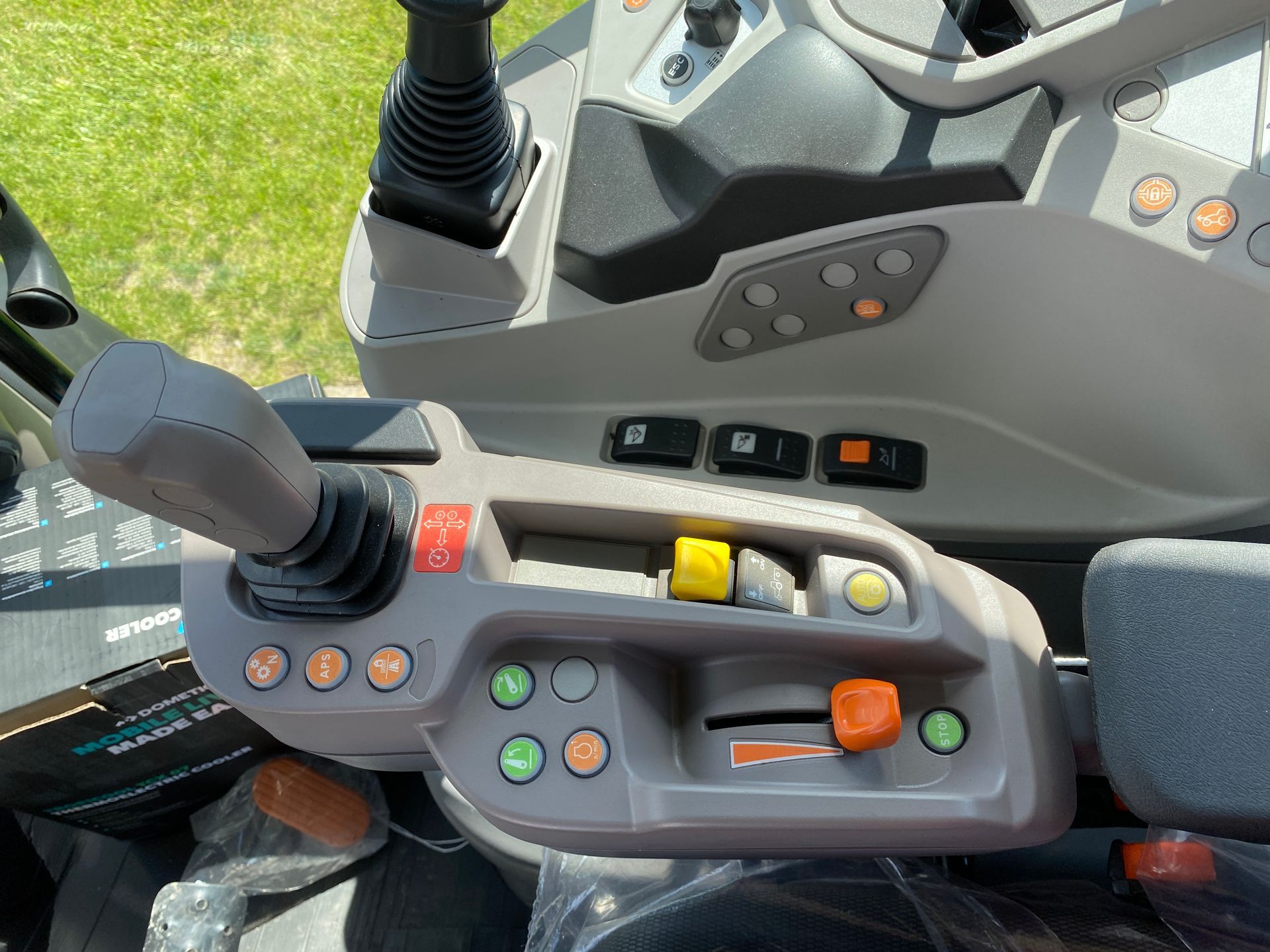Interior of a tractor cab showing controls, including a joystick, buttons, and switches, with a gray and orange color scheme.