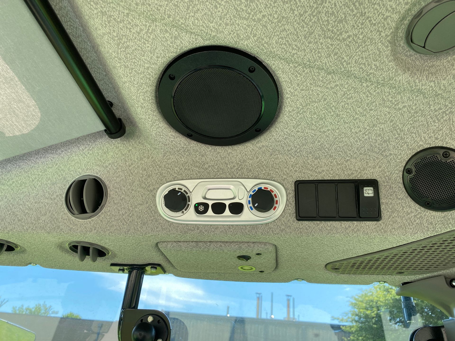 Interior ceiling of a vehicle, showing speakers, vents, and climate control panel.