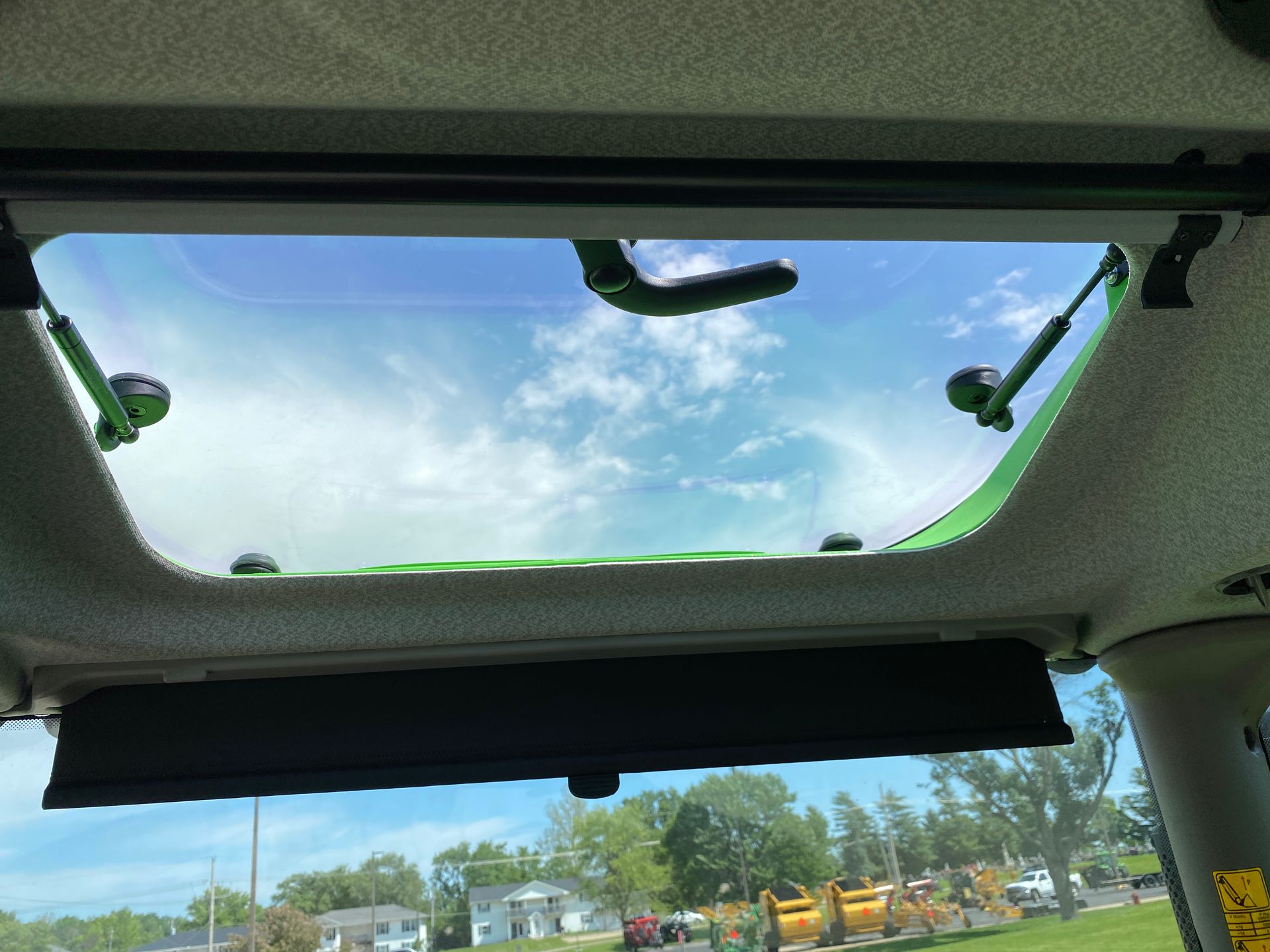 Inside view of a tractor cab with a clear roof panel open to a partly cloudy sky.