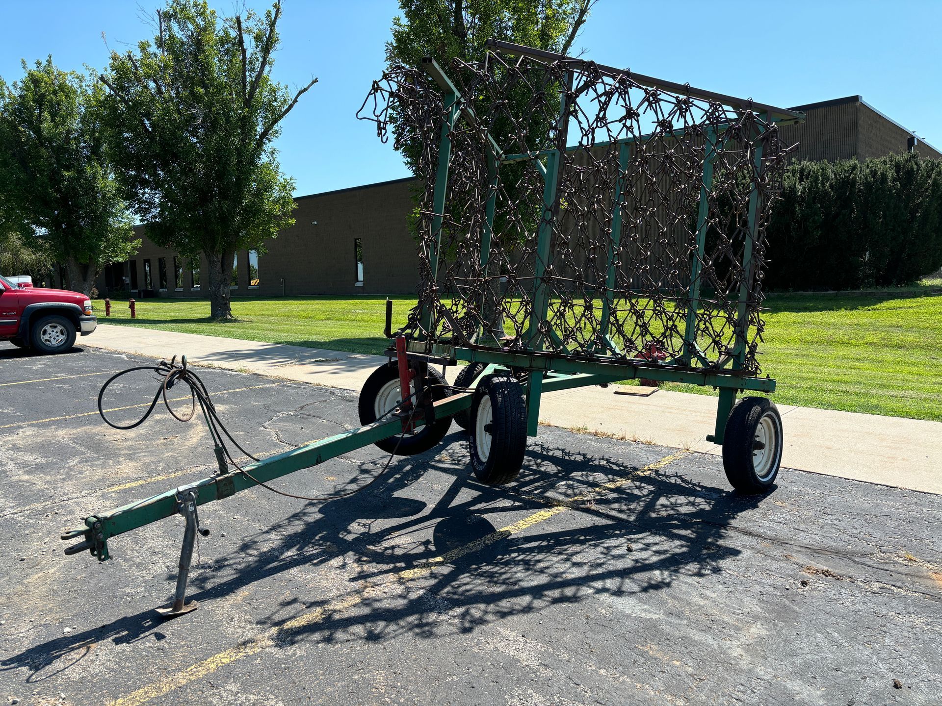 Green harrow with open wire sides, parked on asphalt.