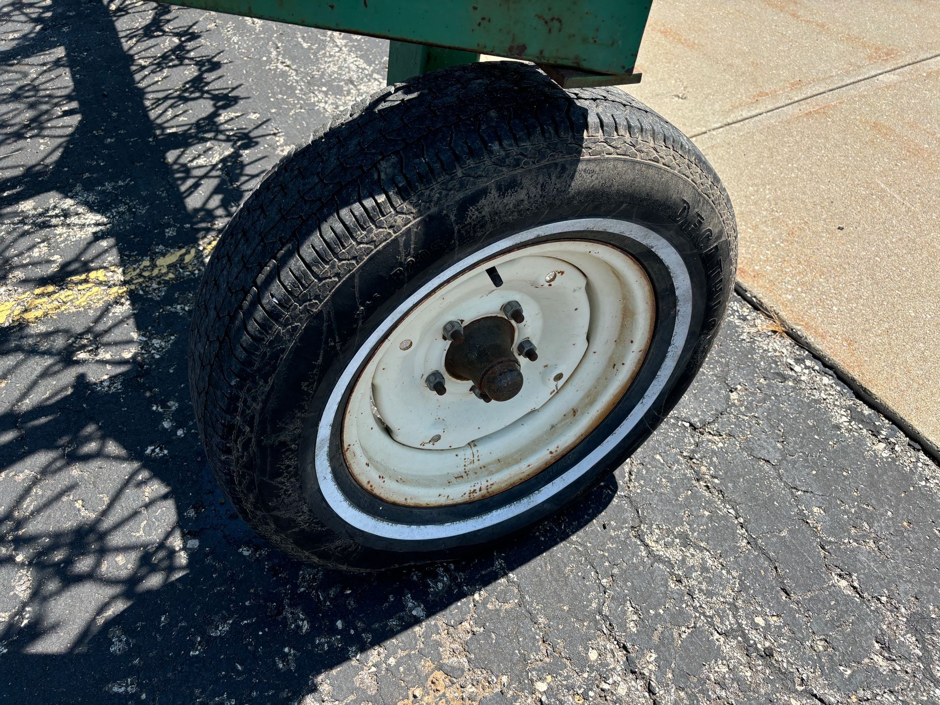 The tire of a green harrow with a white rim on cracked asphalt.