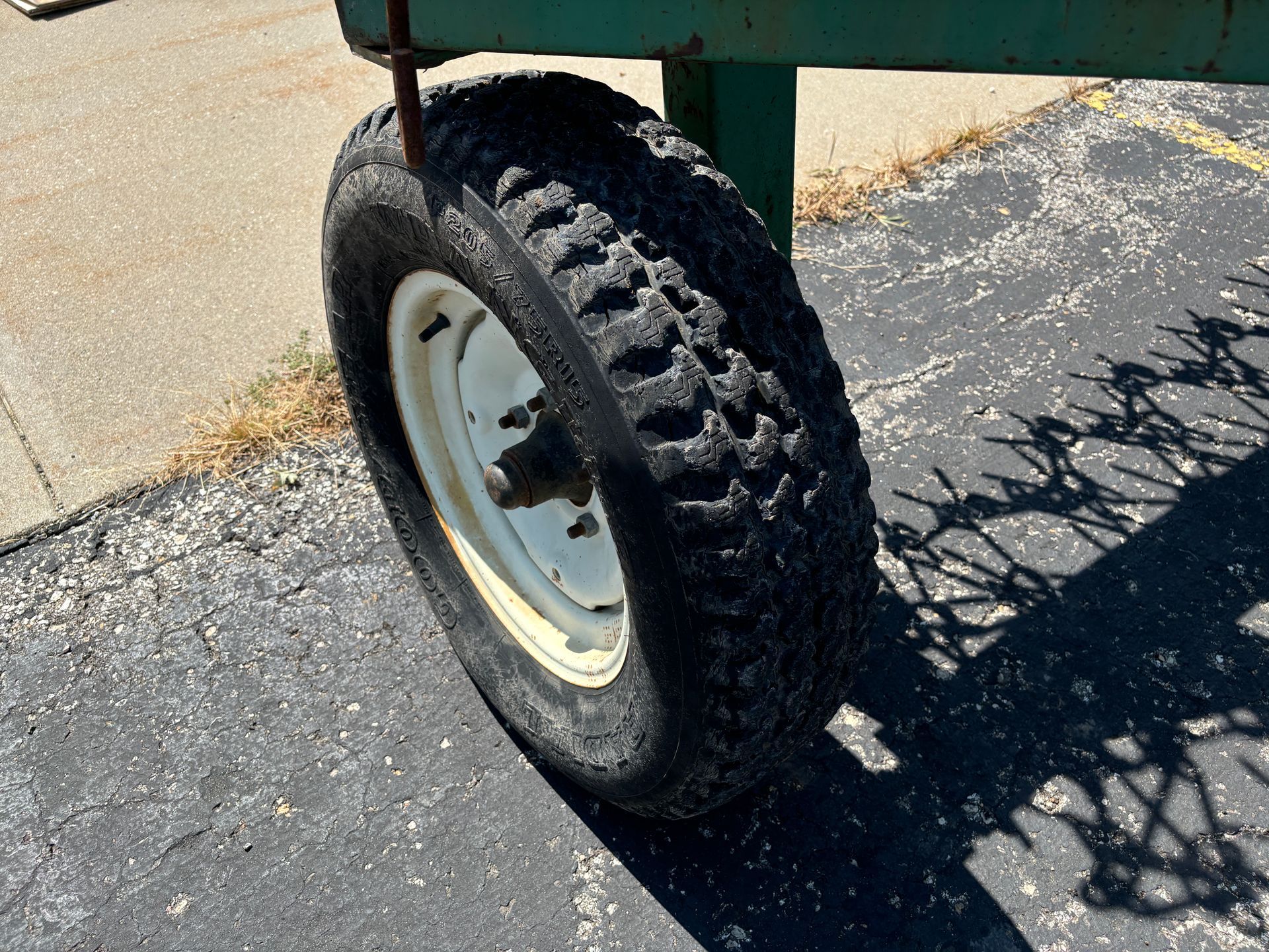 The tire of a green harrow with a white rim on cracked asphalt.