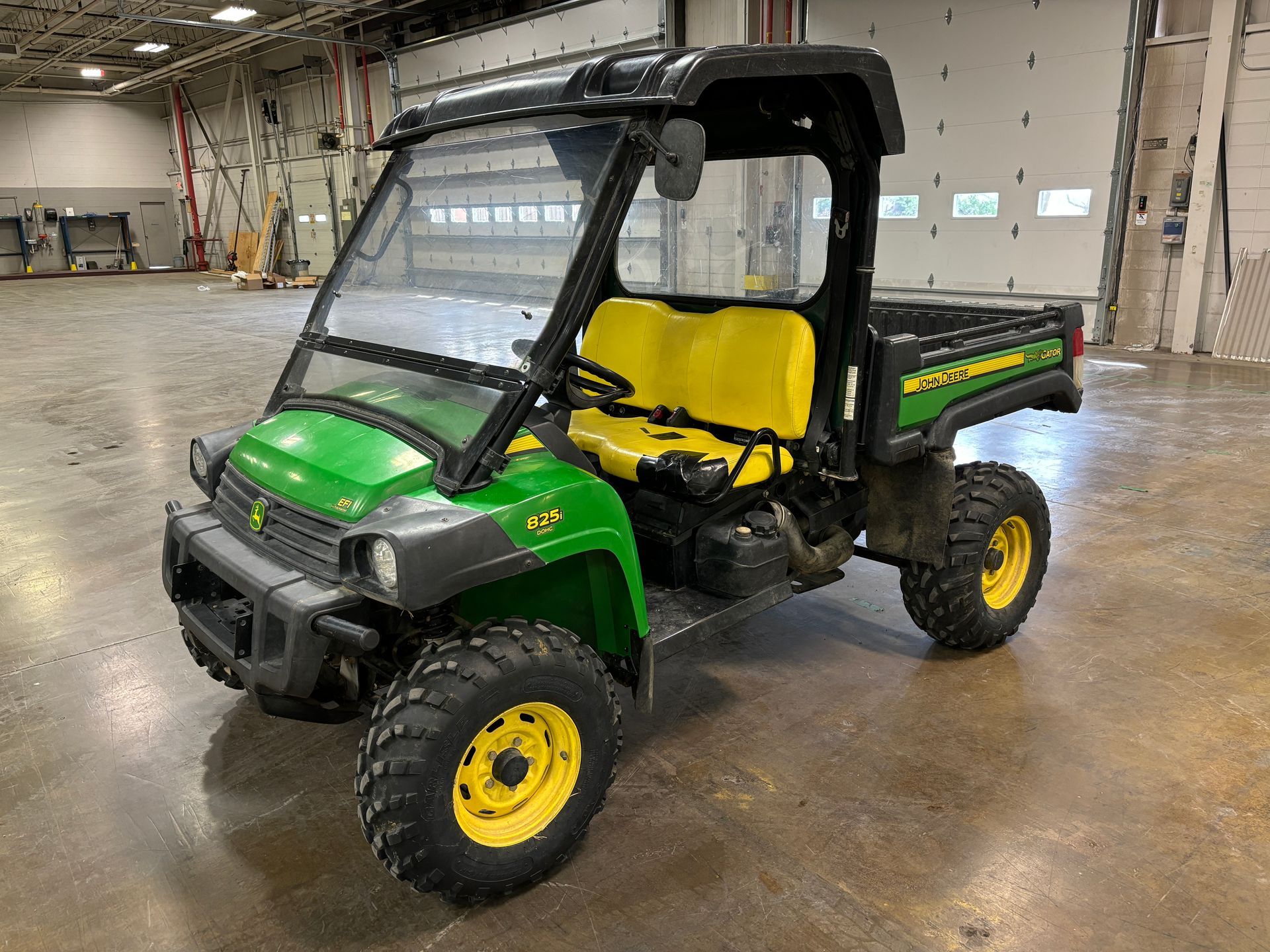 Green and yellow John Deere Gator utility vehicle with a black cab.