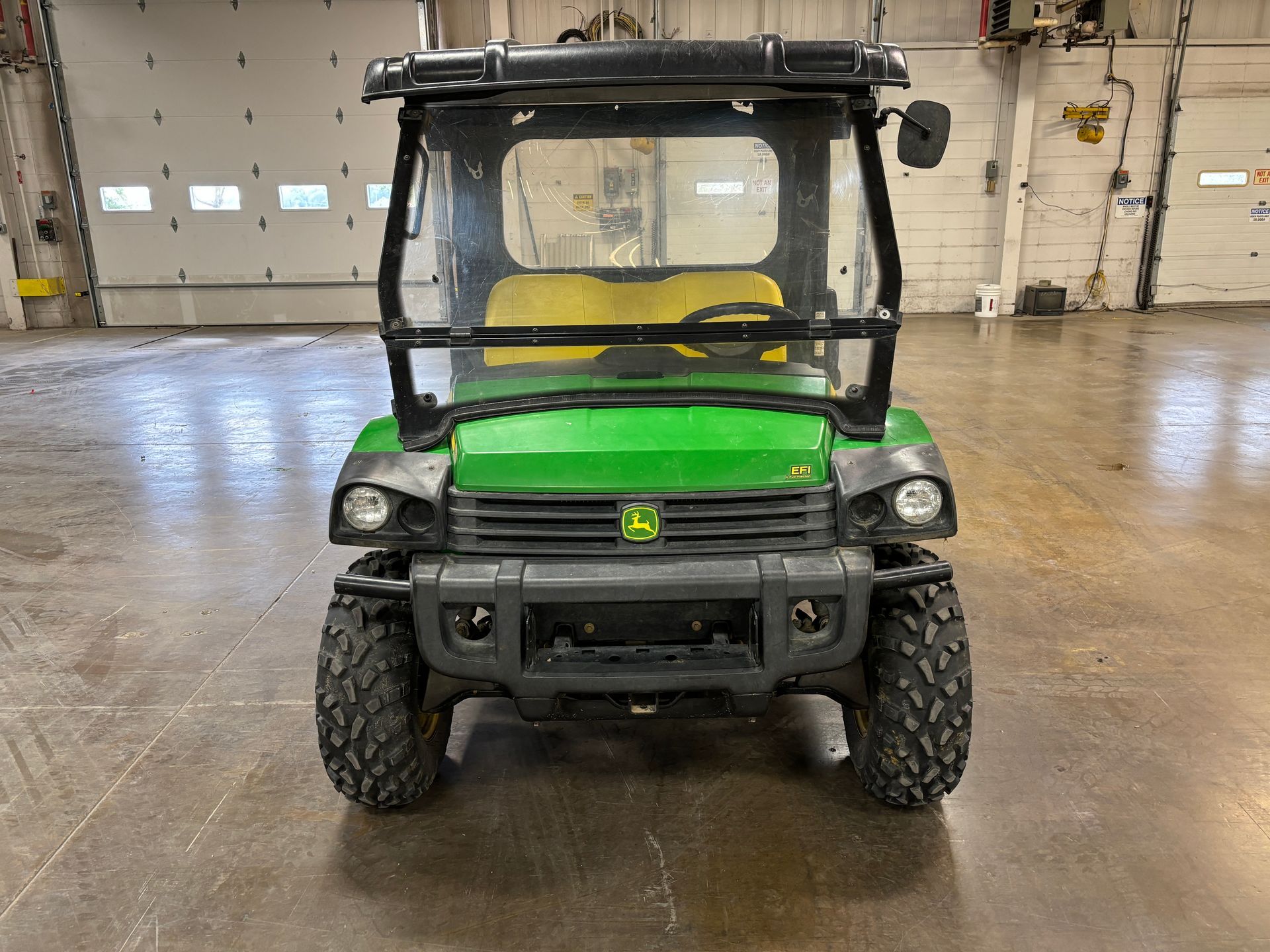 Green John Deere utility vehicle with a black roof and clear windshield in a garage.
