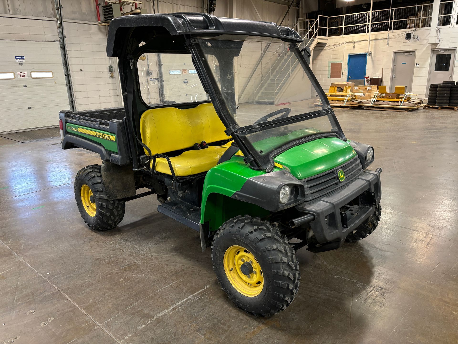 John Deere Gator utility vehicle with a black cab, yellow seats, and large tires.