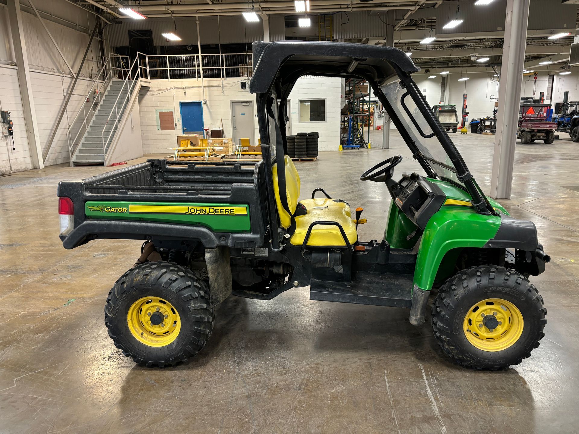 John Deere Gator utility vehicle, green and yellow, in a warehouse setting.