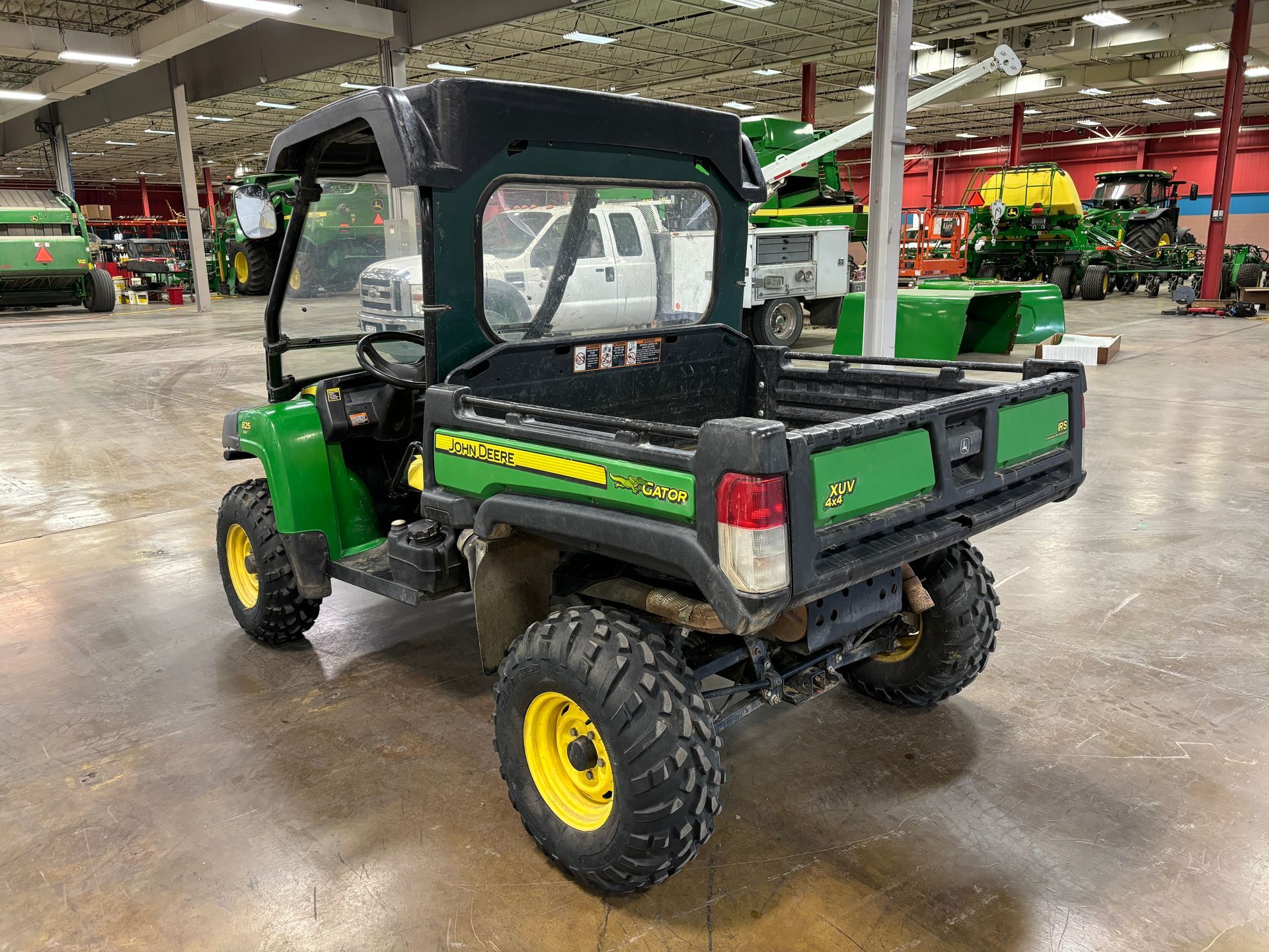 Green John Deere utility vehicle with black canopy, rear view.