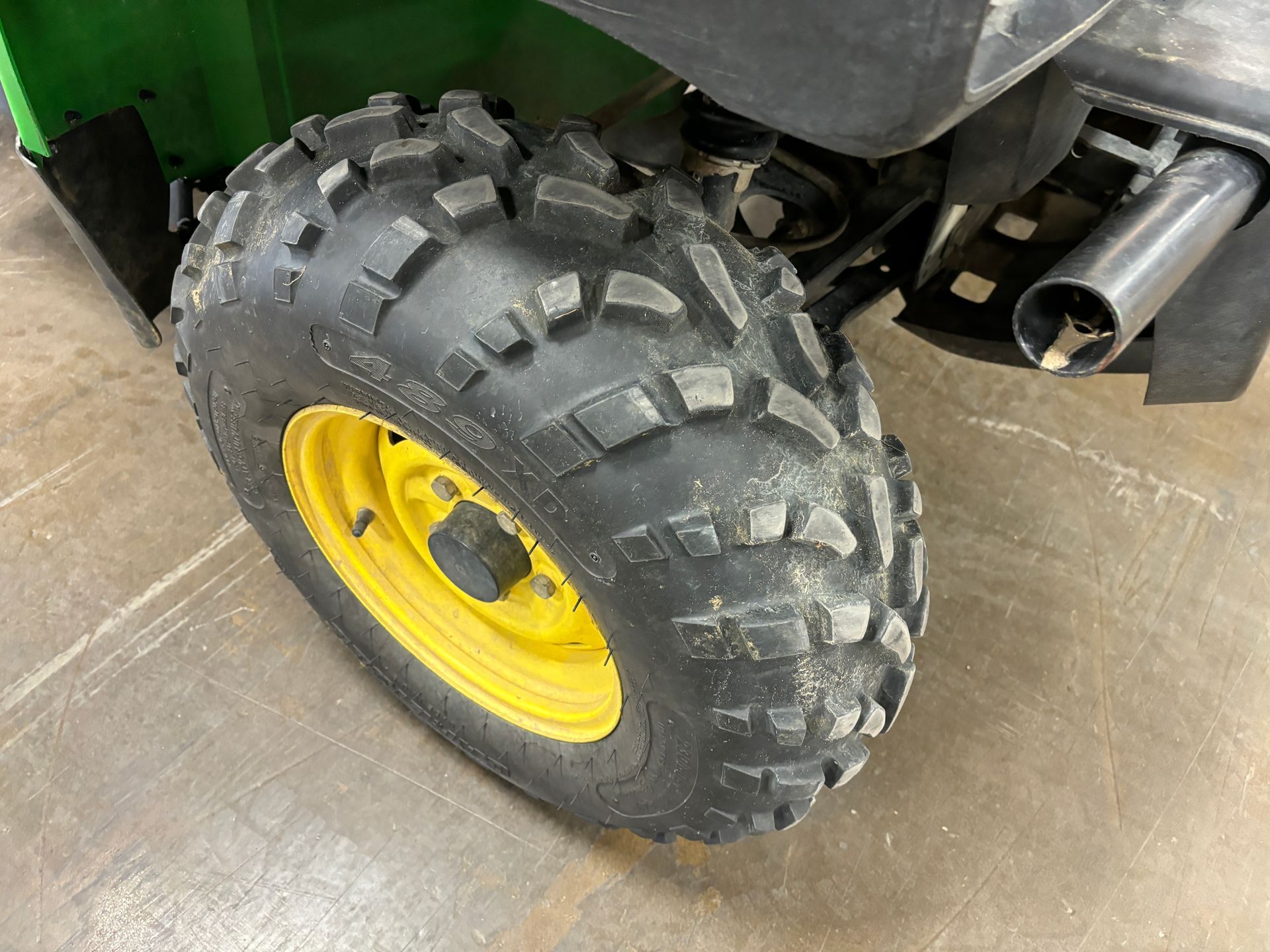 Close-up of a John Deere UTV wheel and tire; the wheel is yellow, and the tire is black with a rugged tread.