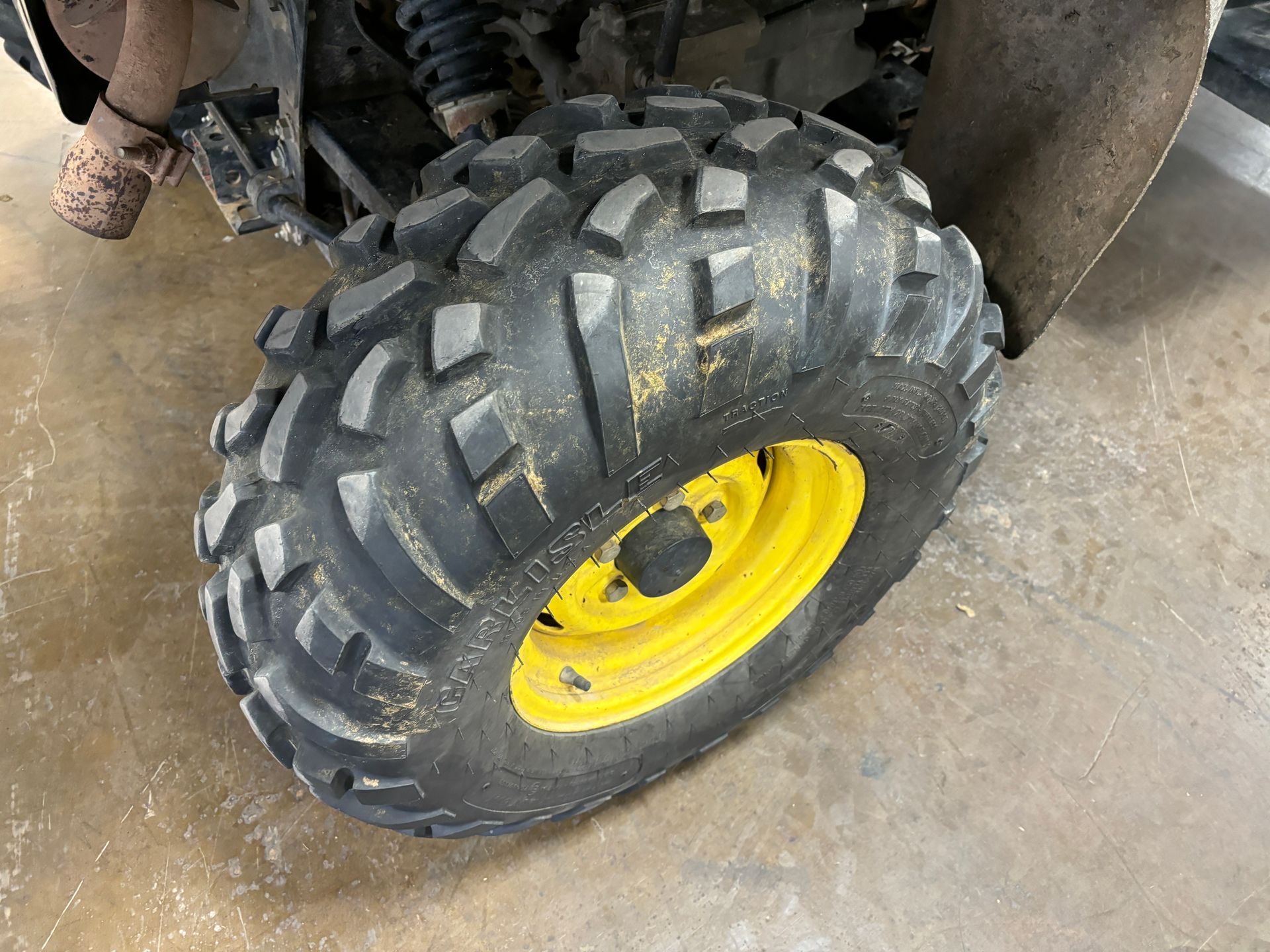 Close-up of a John Deere ATV tire with a yellow rim on a concrete floor.