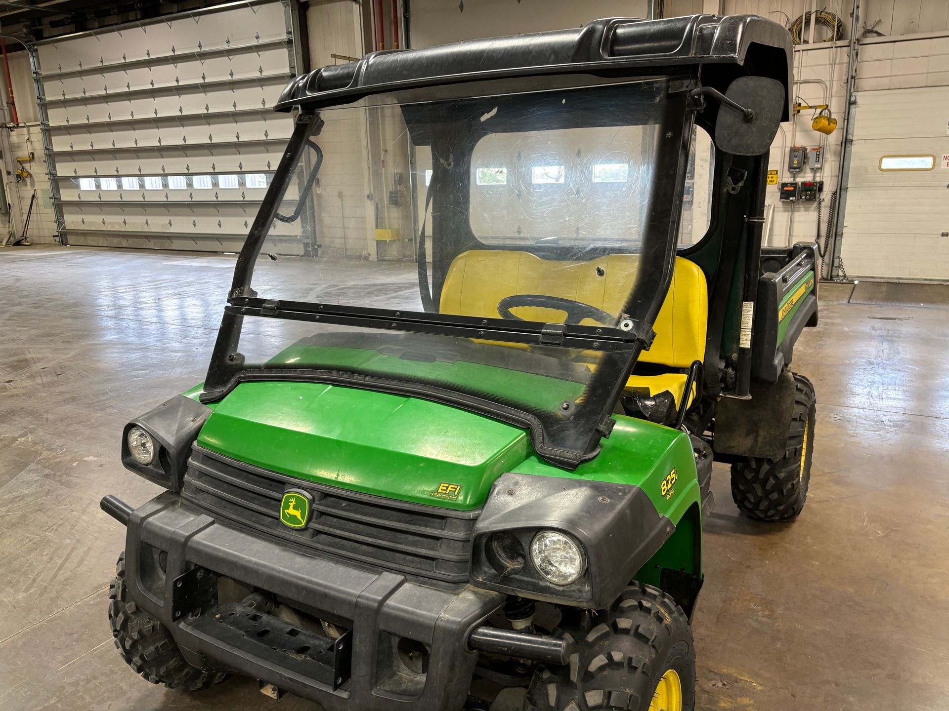 Green and black John Deere utility vehicle with a windshield and canopy inside a building.